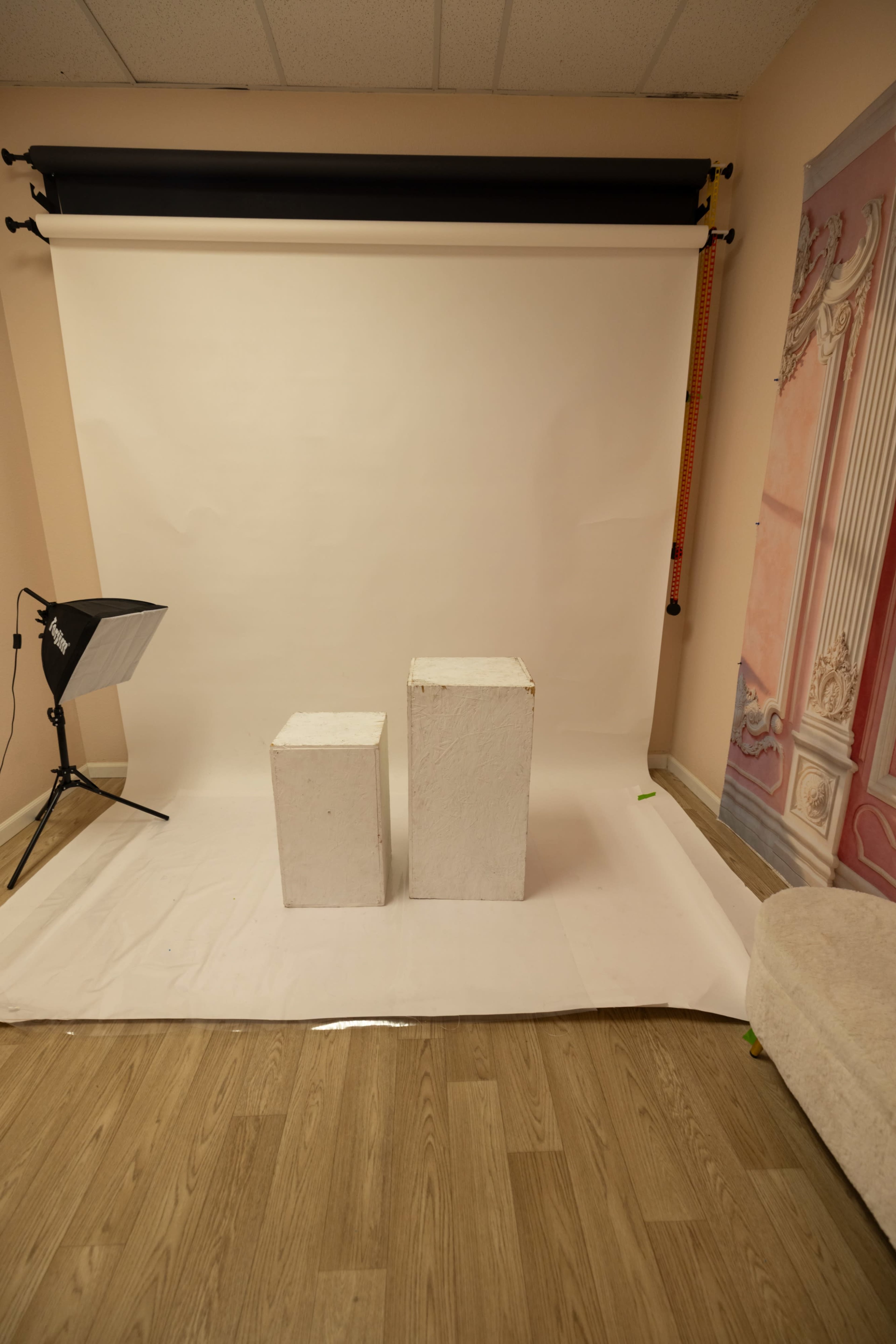 The image shows a photo studio setup with two white pedestals on a plain backdrop and a lighting equipment on the side.