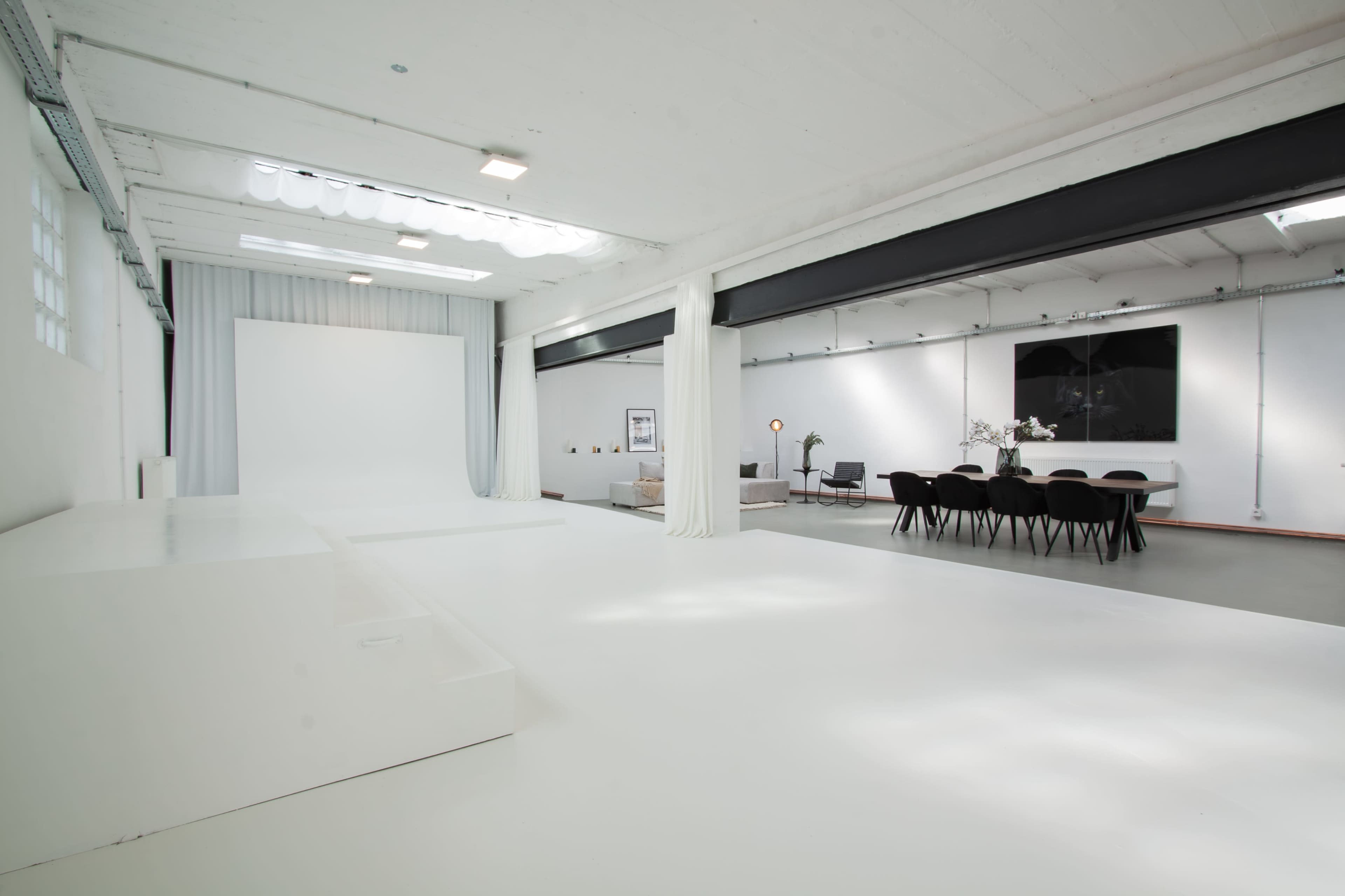A spacious, modern interior with a white floor, a blank backdrop, and a dining area featuring a table and chairs.