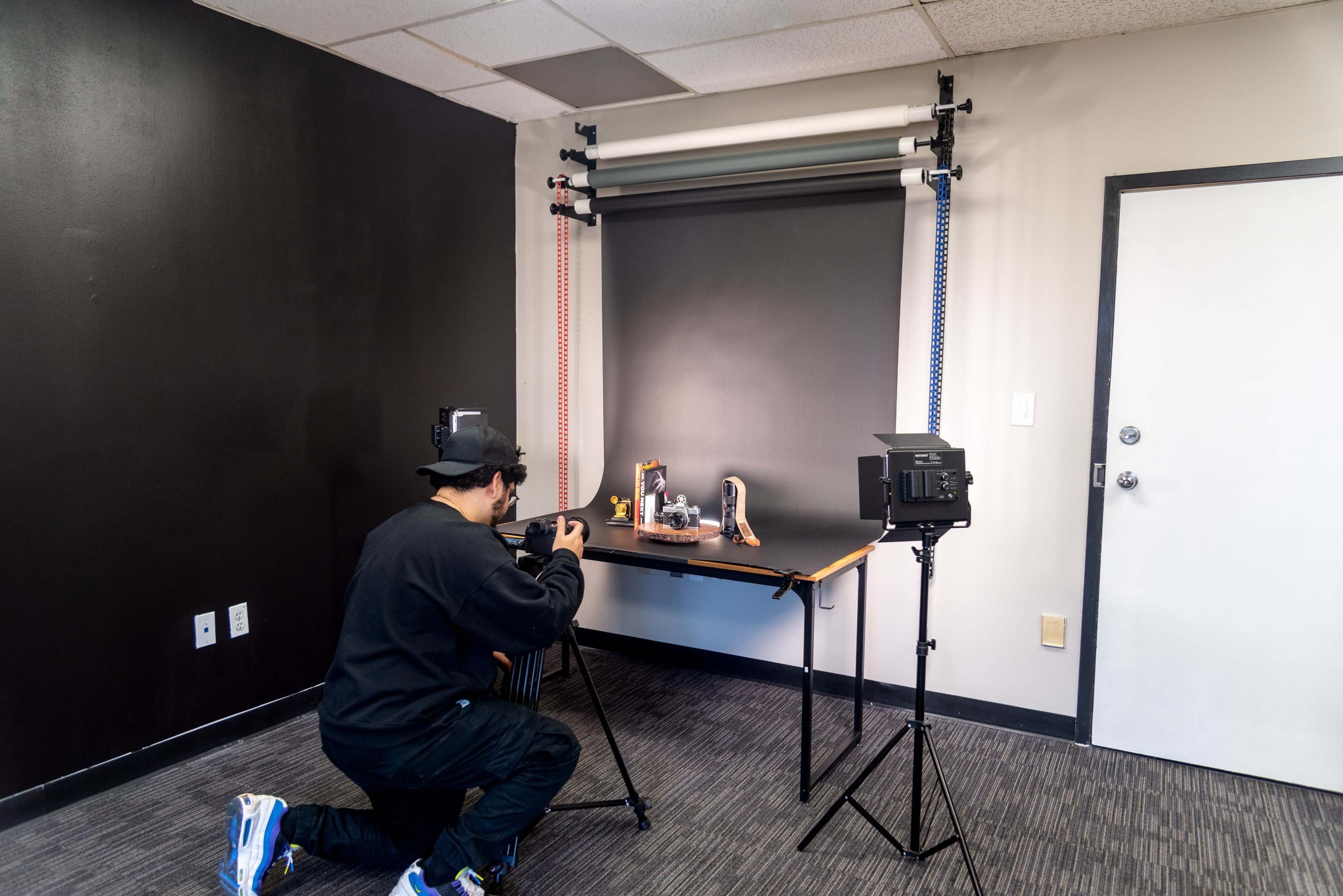 A person is kneeling while taking photographs of various items displayed on a table in a studio setting.