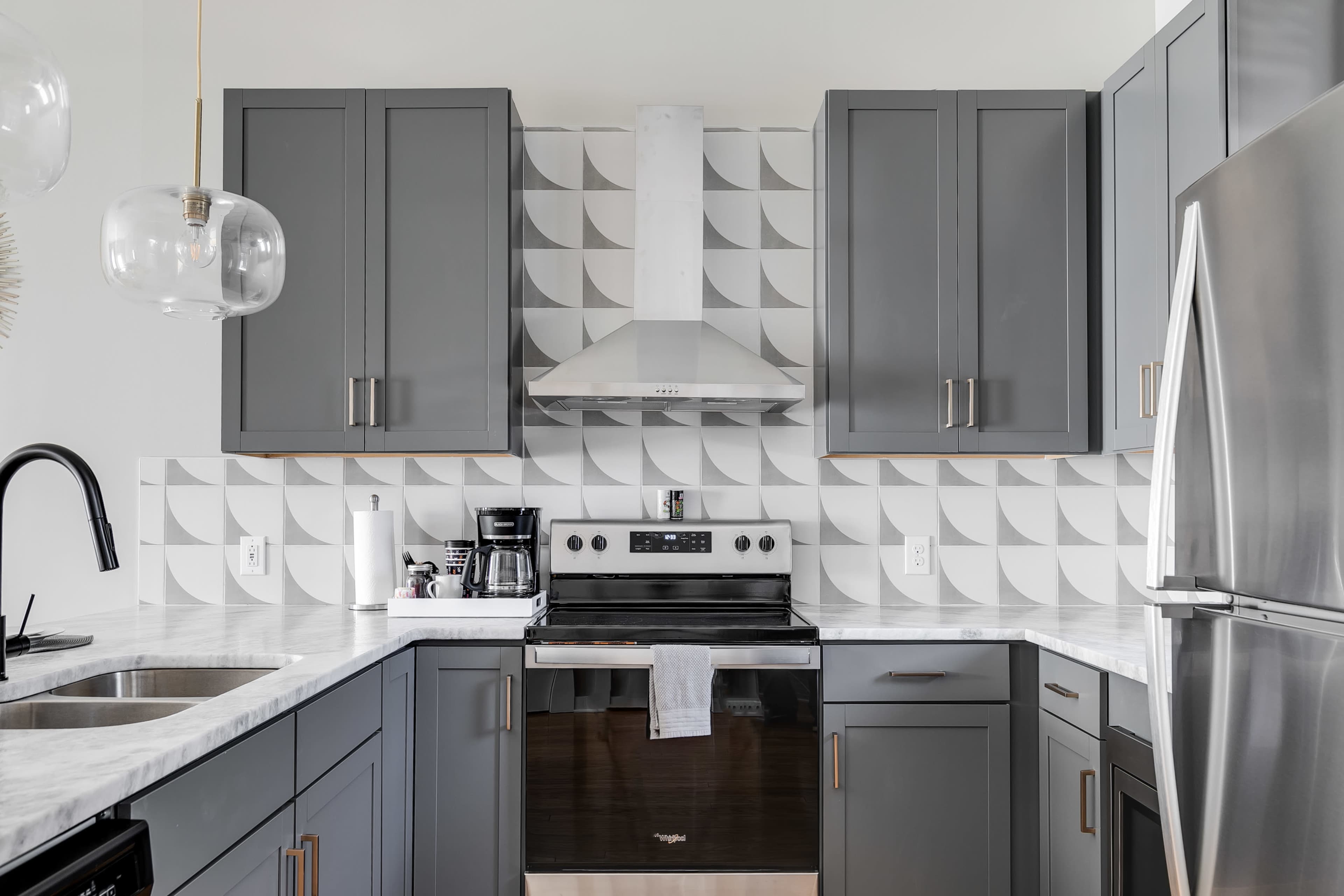 A modern kitchen with gray cabinets, a stainless steel stove, and distinctive patterned backsplash tiles.