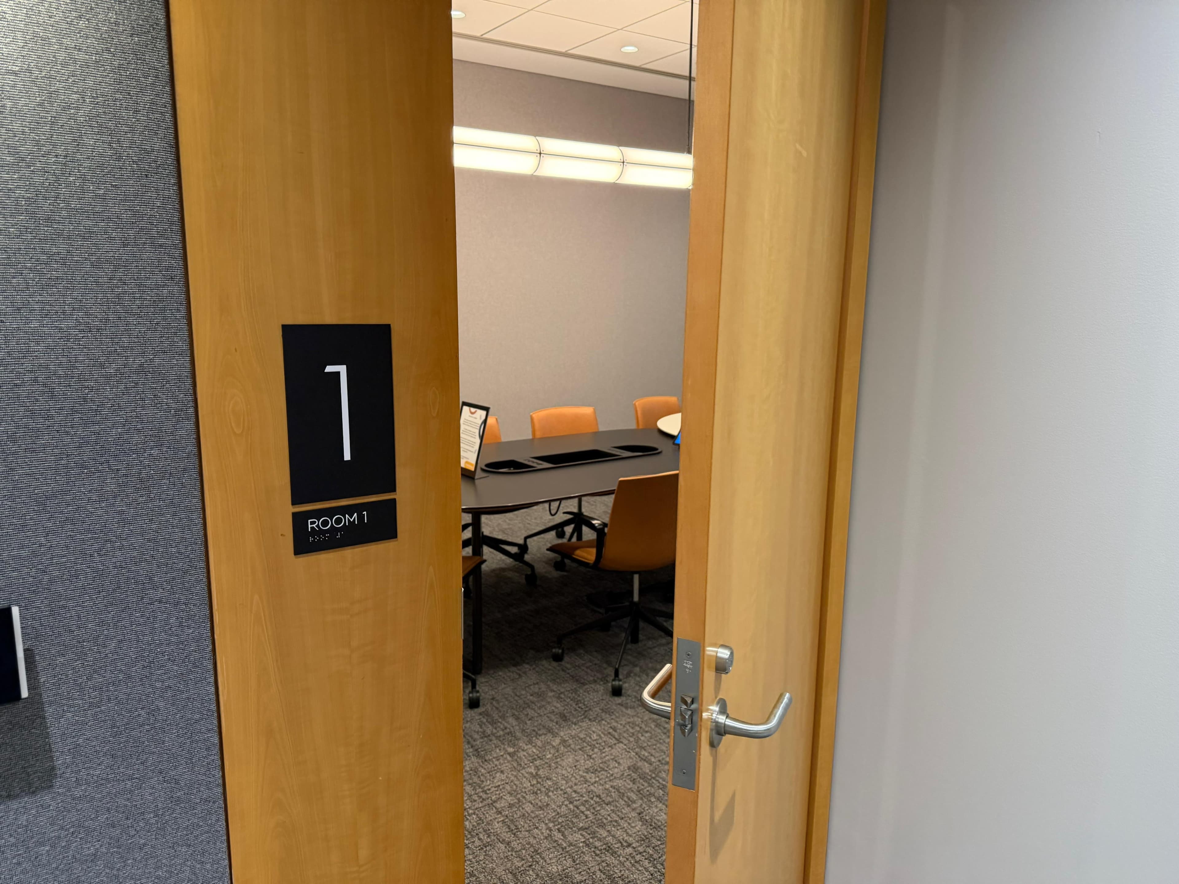 A conference room labeled "Room 1" is partially visible through an open wooden door, showing a table surrounded by chairs.
