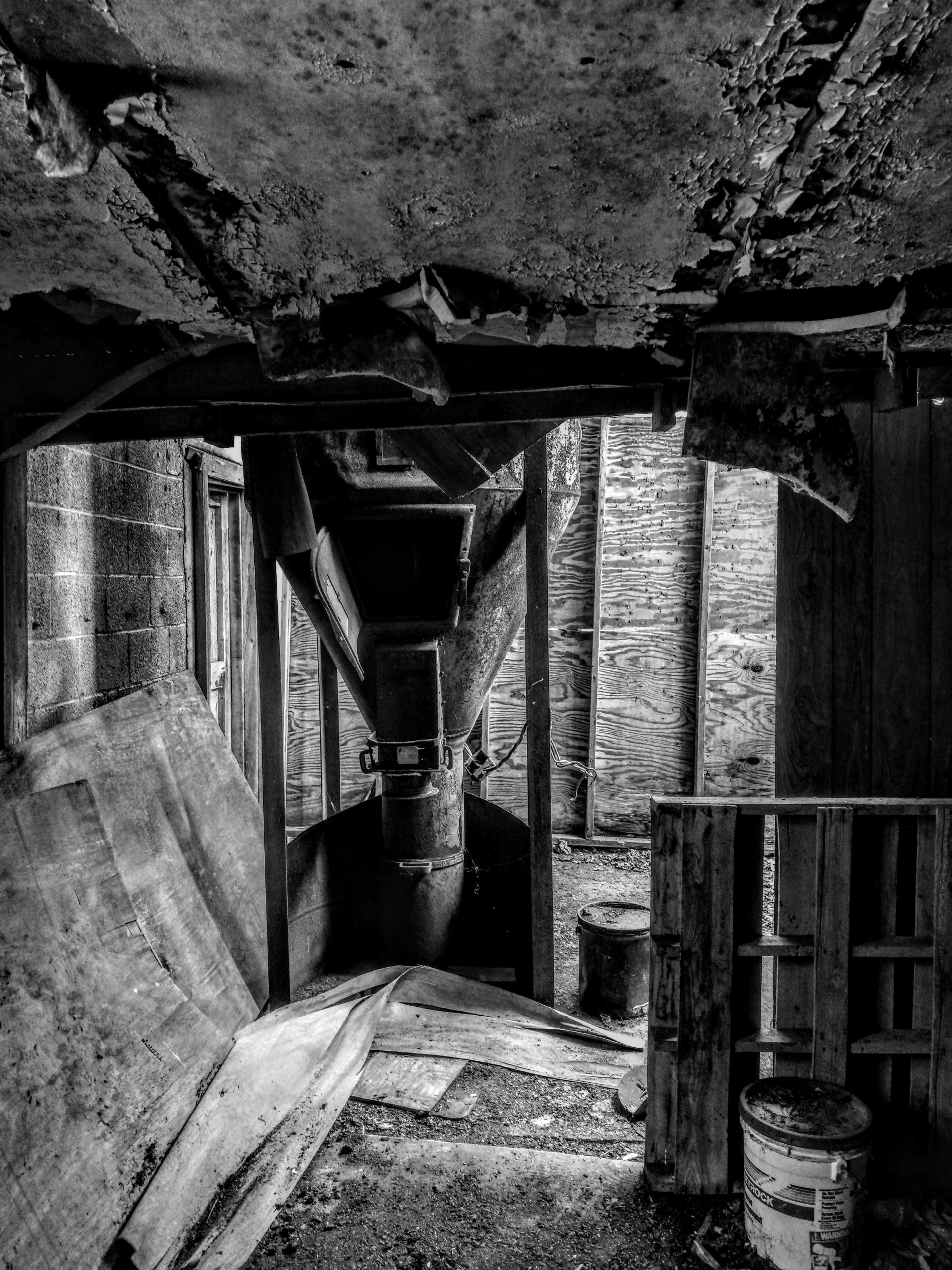An industrial area features a large, rusty machine under a peeling ceiling with wooden pallets and scattered debris on the floor.