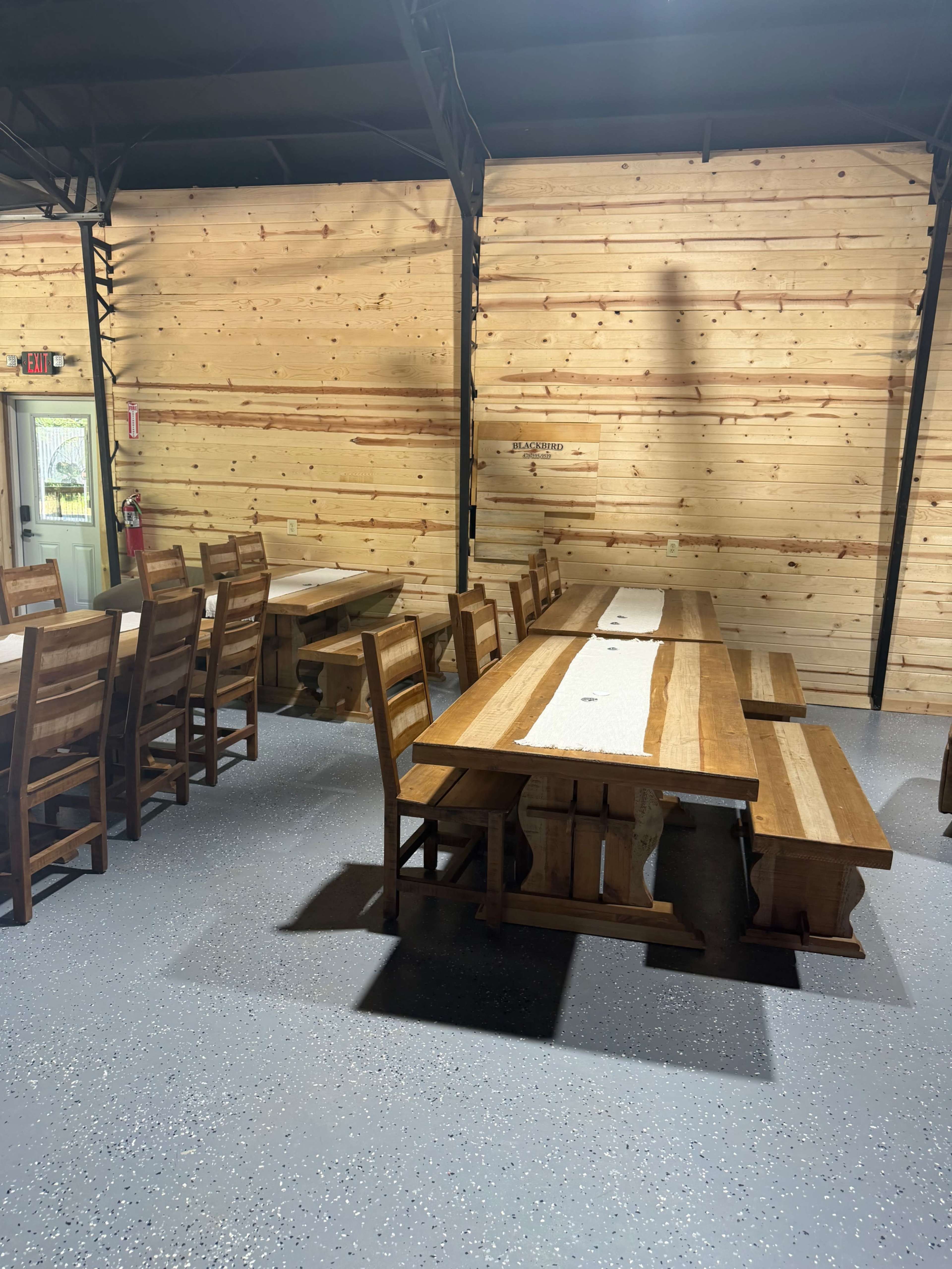 The image shows a spacious dining area with wooden tables and chairs against a backdrop of wooden walls.