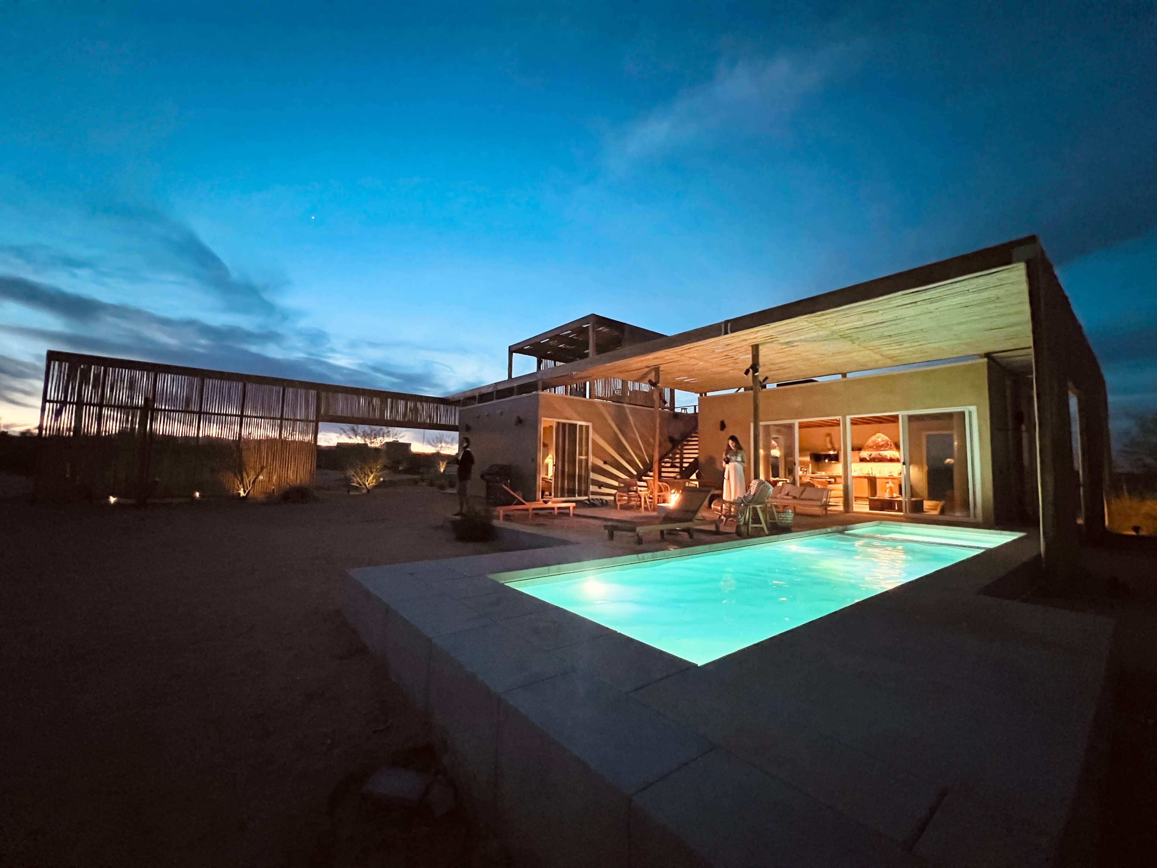 A modern building with a pool is illuminated at night under a blue sky.