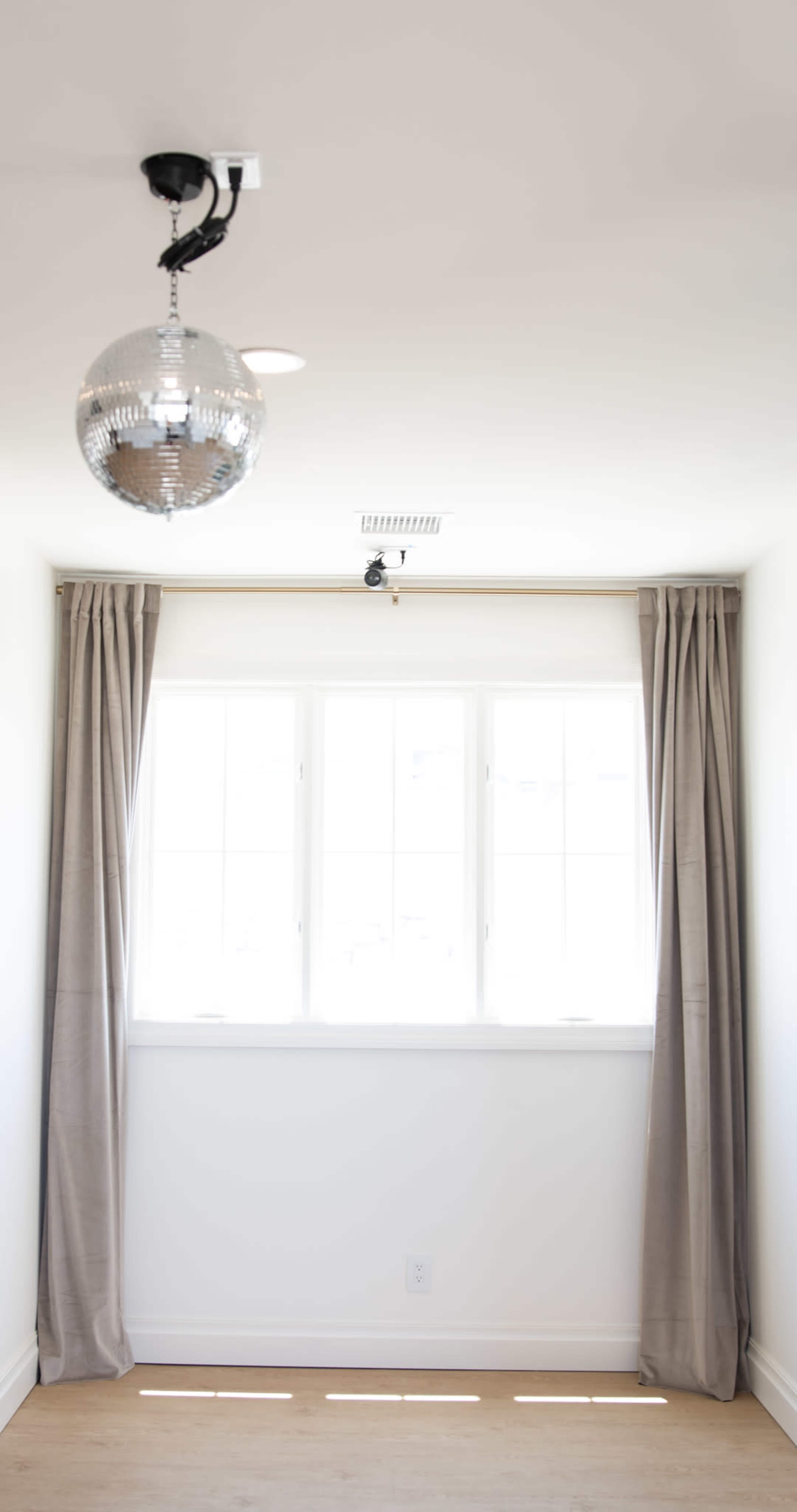 The image shows a room with a window, beige curtains, and a mirrored disco ball hanging from the ceiling.