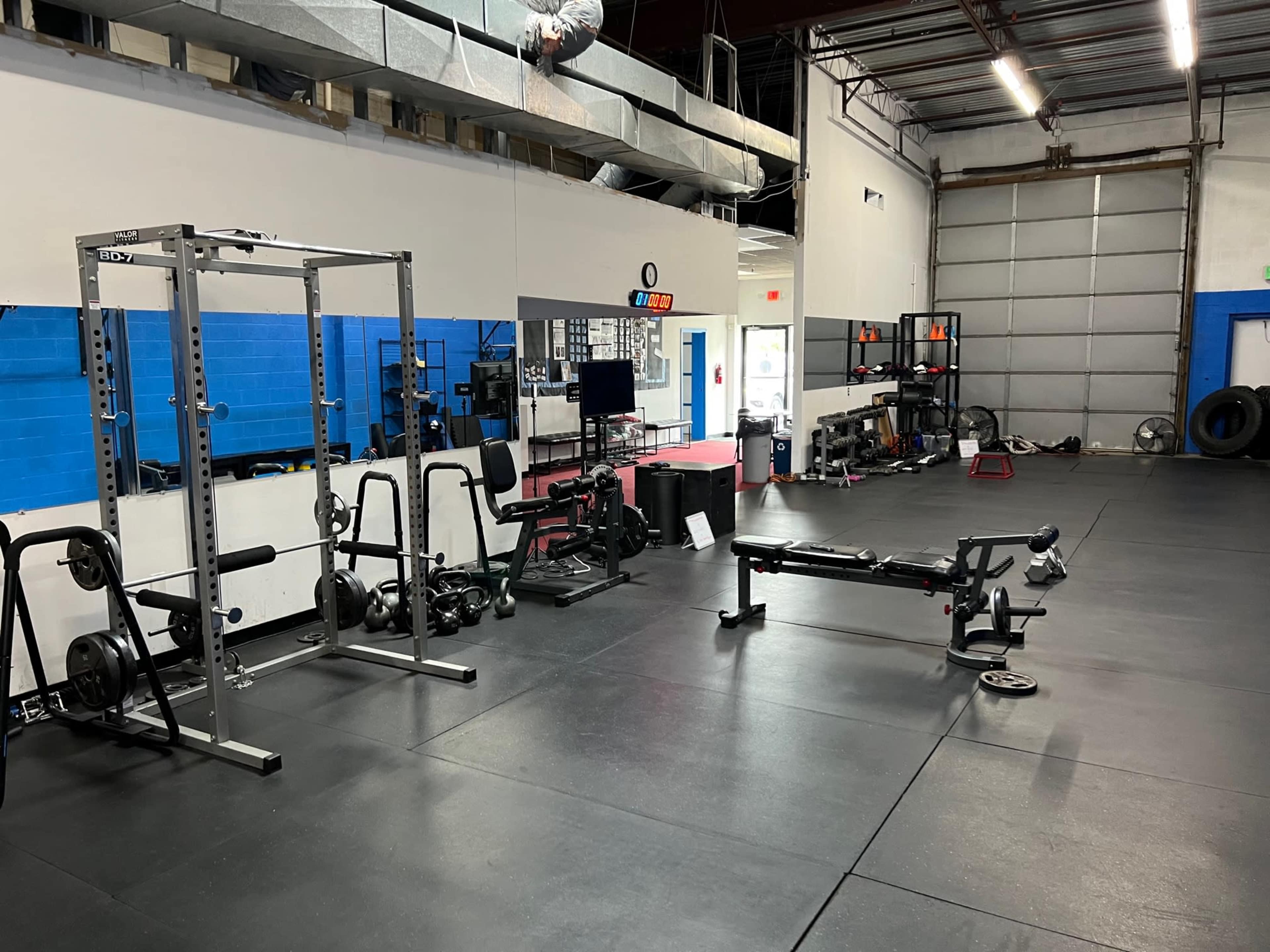 A gym interior with weightlifting equipment, mirrors, and a spacious workout area with black flooring.