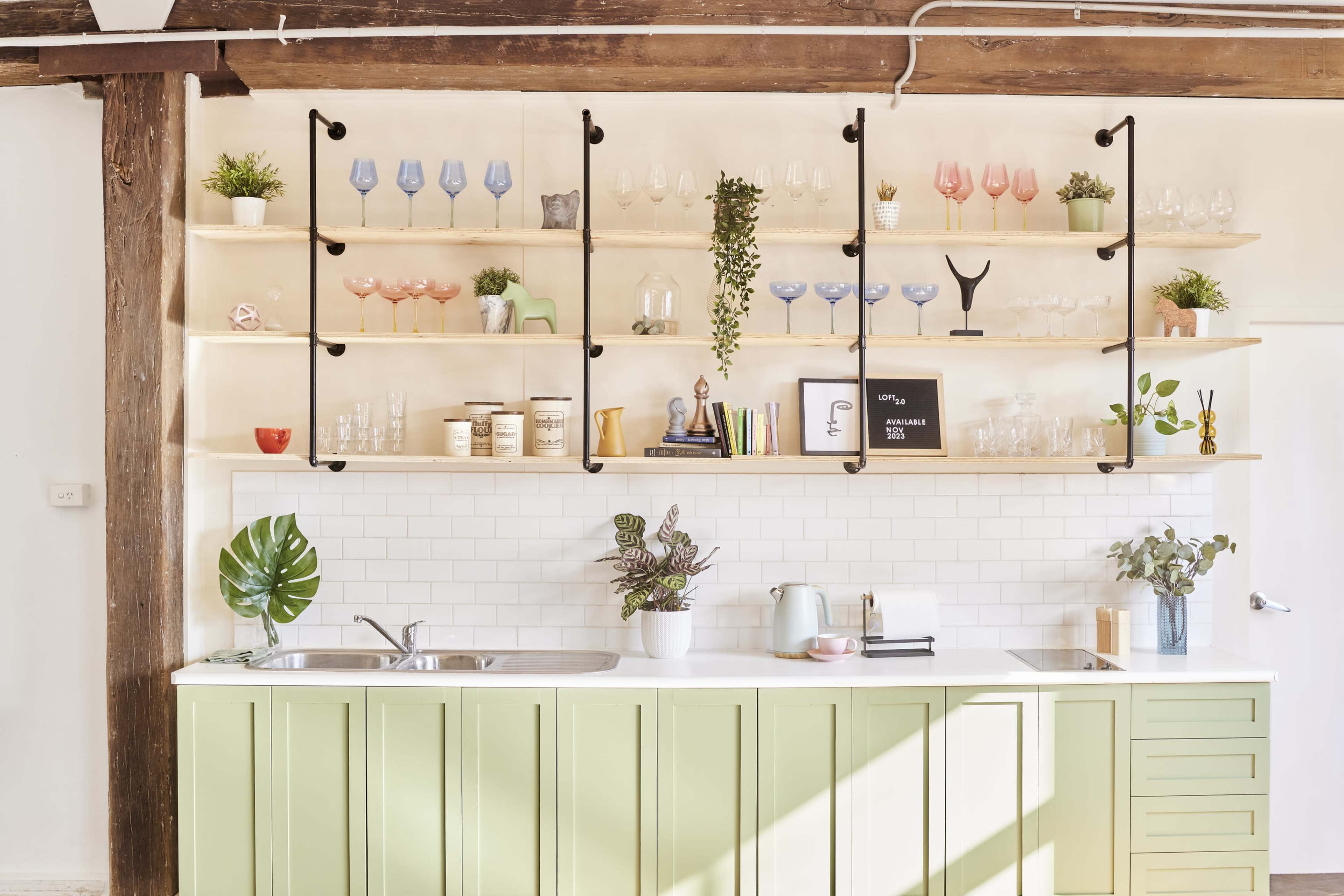 A kitchen with a green cabinetry, a white countertop, and open shelves displaying various glassware and decorative items.