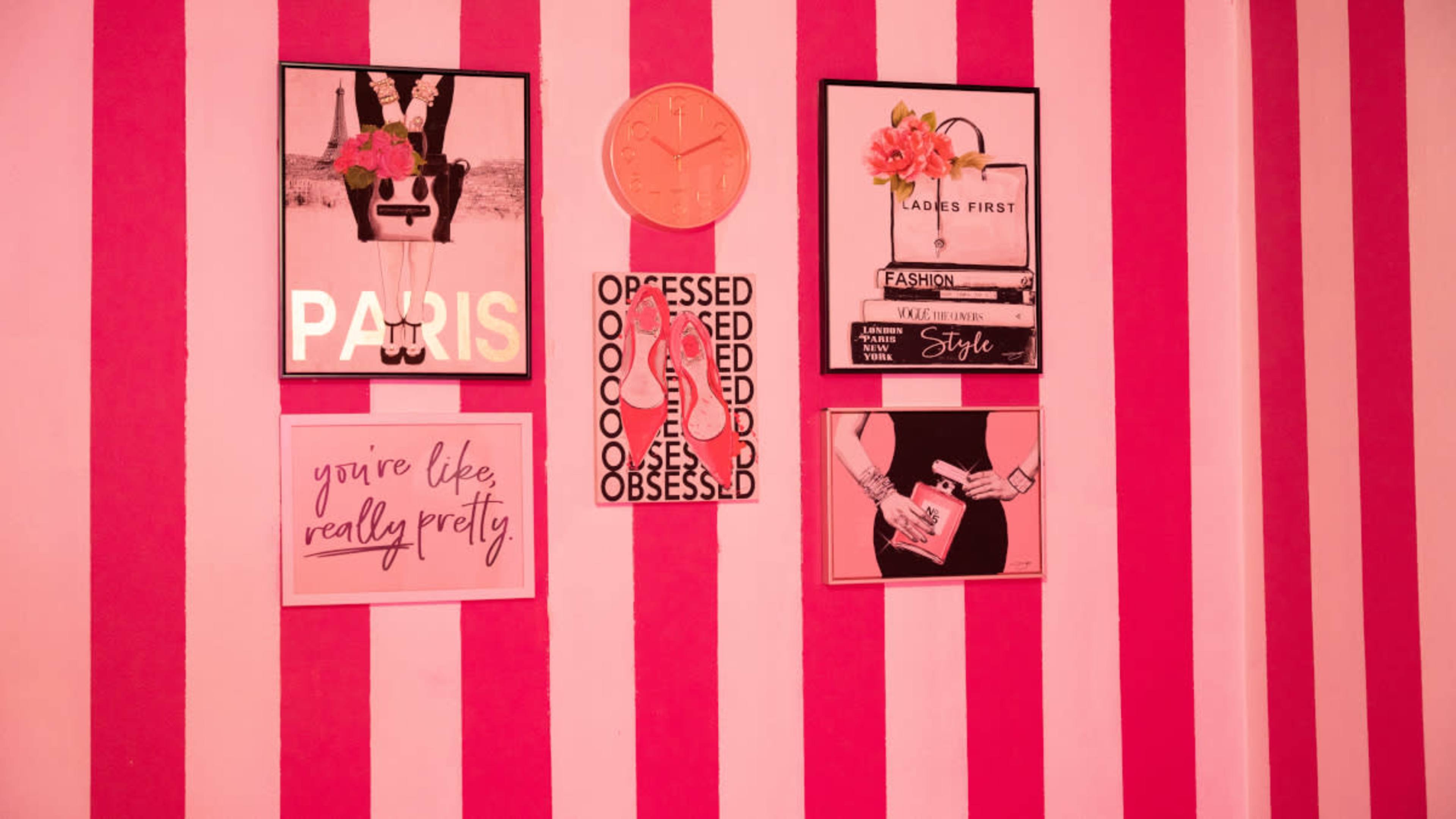 The image features a pink-striped wall with various framed artworks and motivational quotes arranged on it.