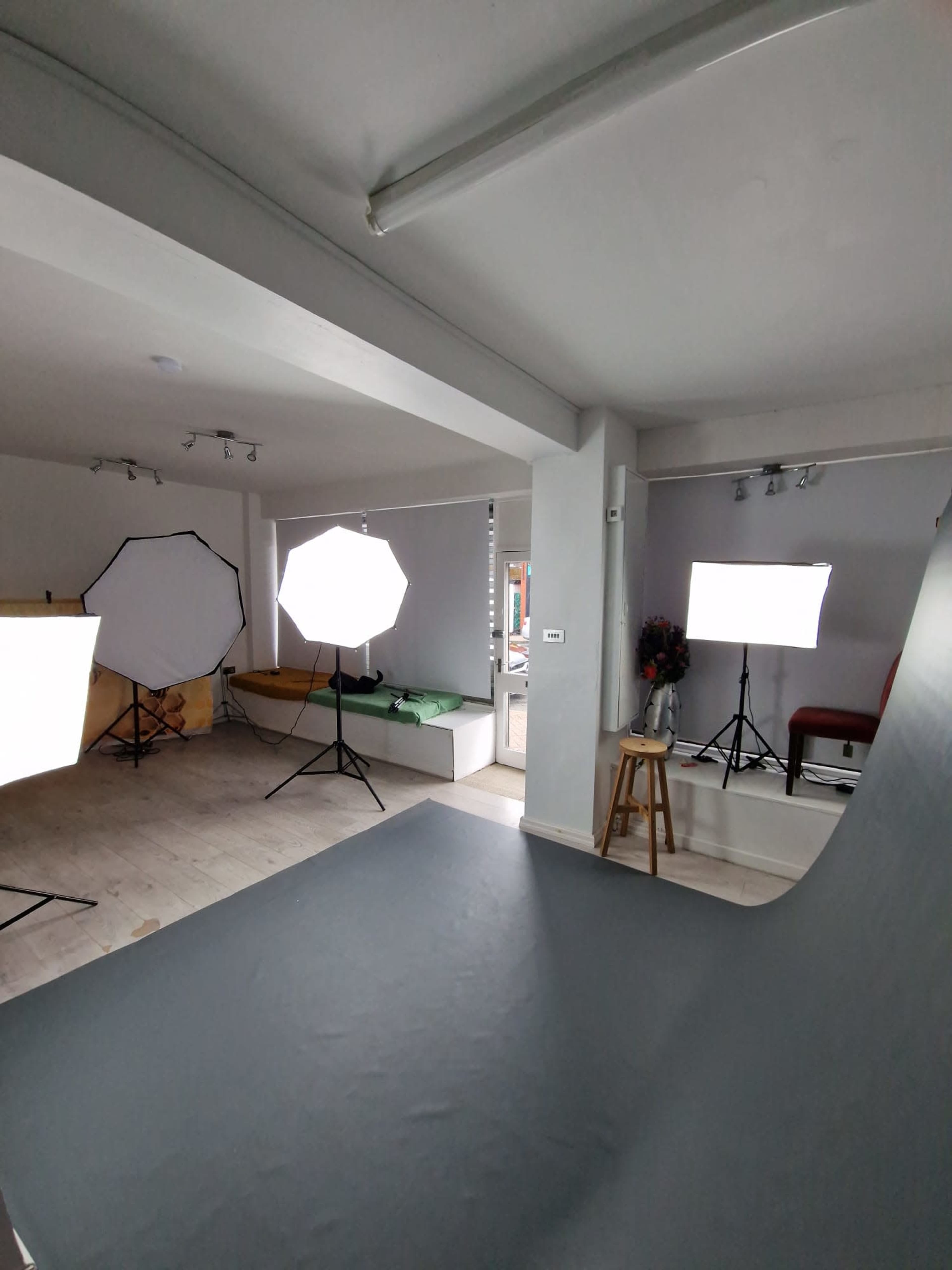 The image shows a photography studio equipped with several light sources, a backdrop, and a few furnishings.