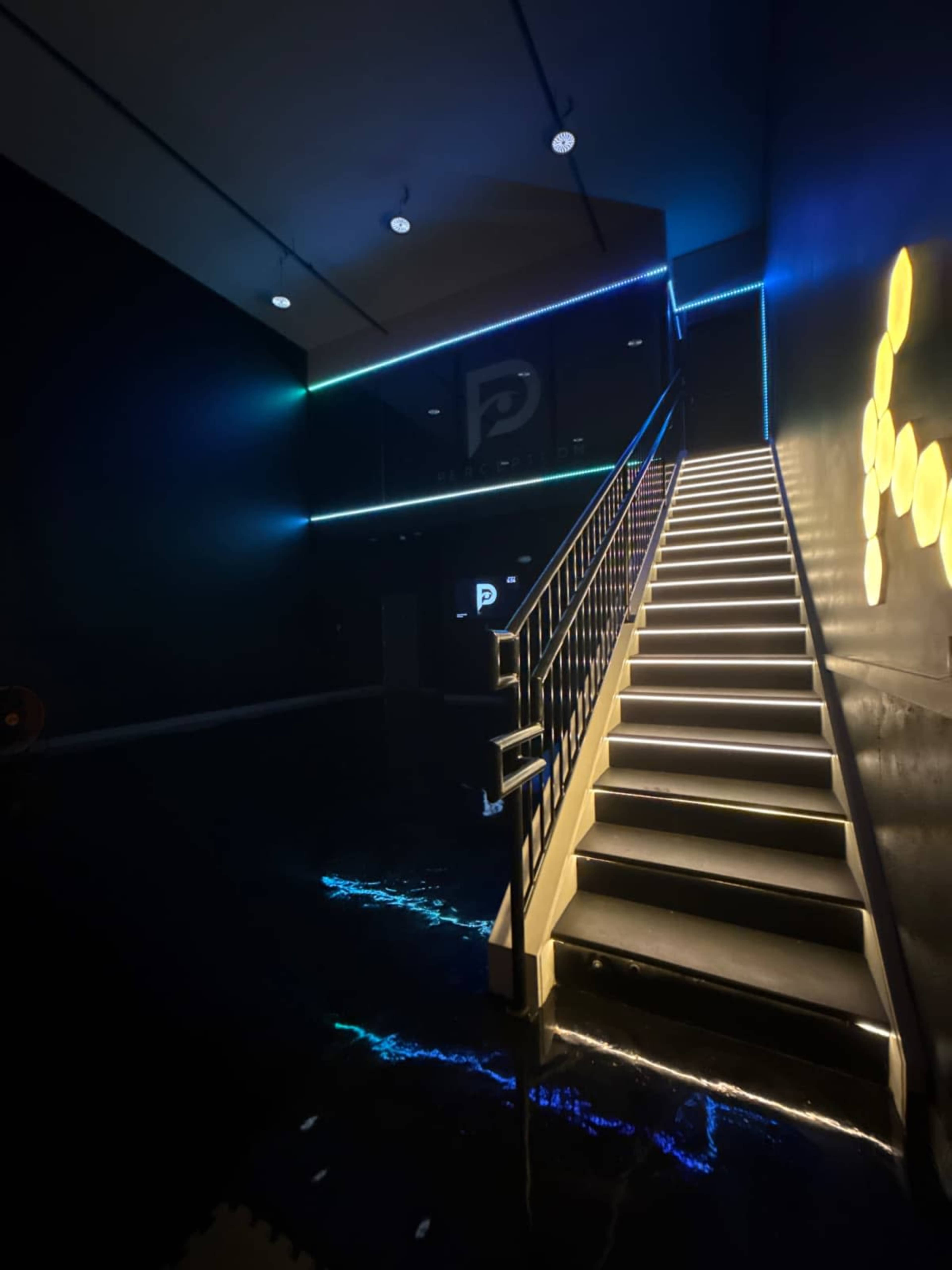 The image shows a staircase illuminated by LED lights in a dark room, with a modern design and sleek walls.