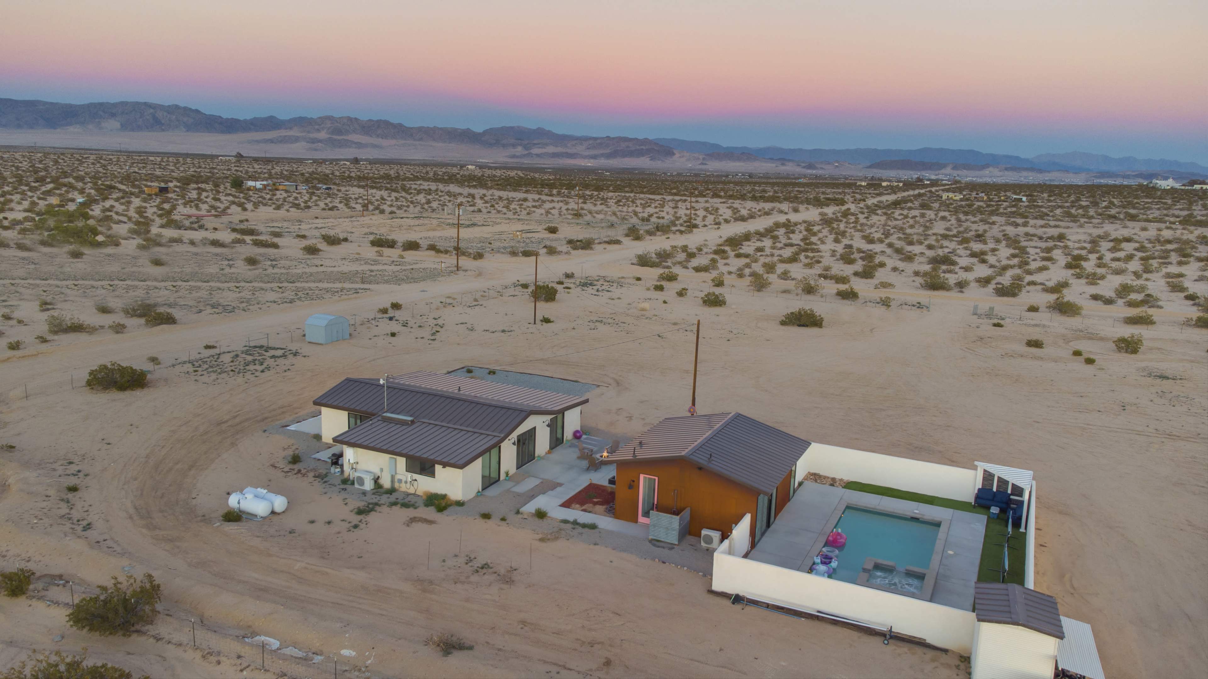 Aerial view of a small residential complex with two houses and a pool set in a desert landscape.