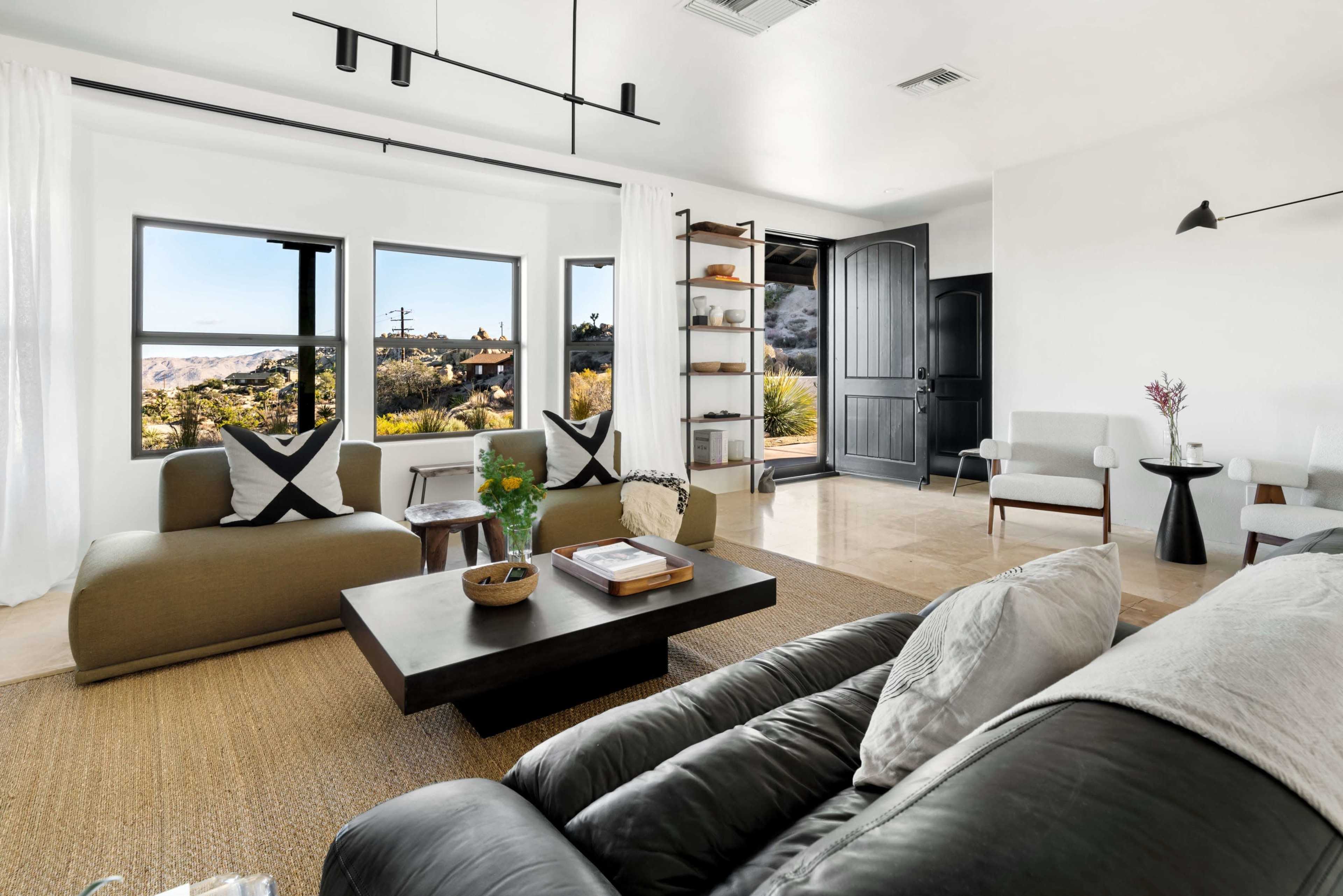 A modern living room features large windows with a view, minimalist furniture, and a mix of natural and neutral colors.