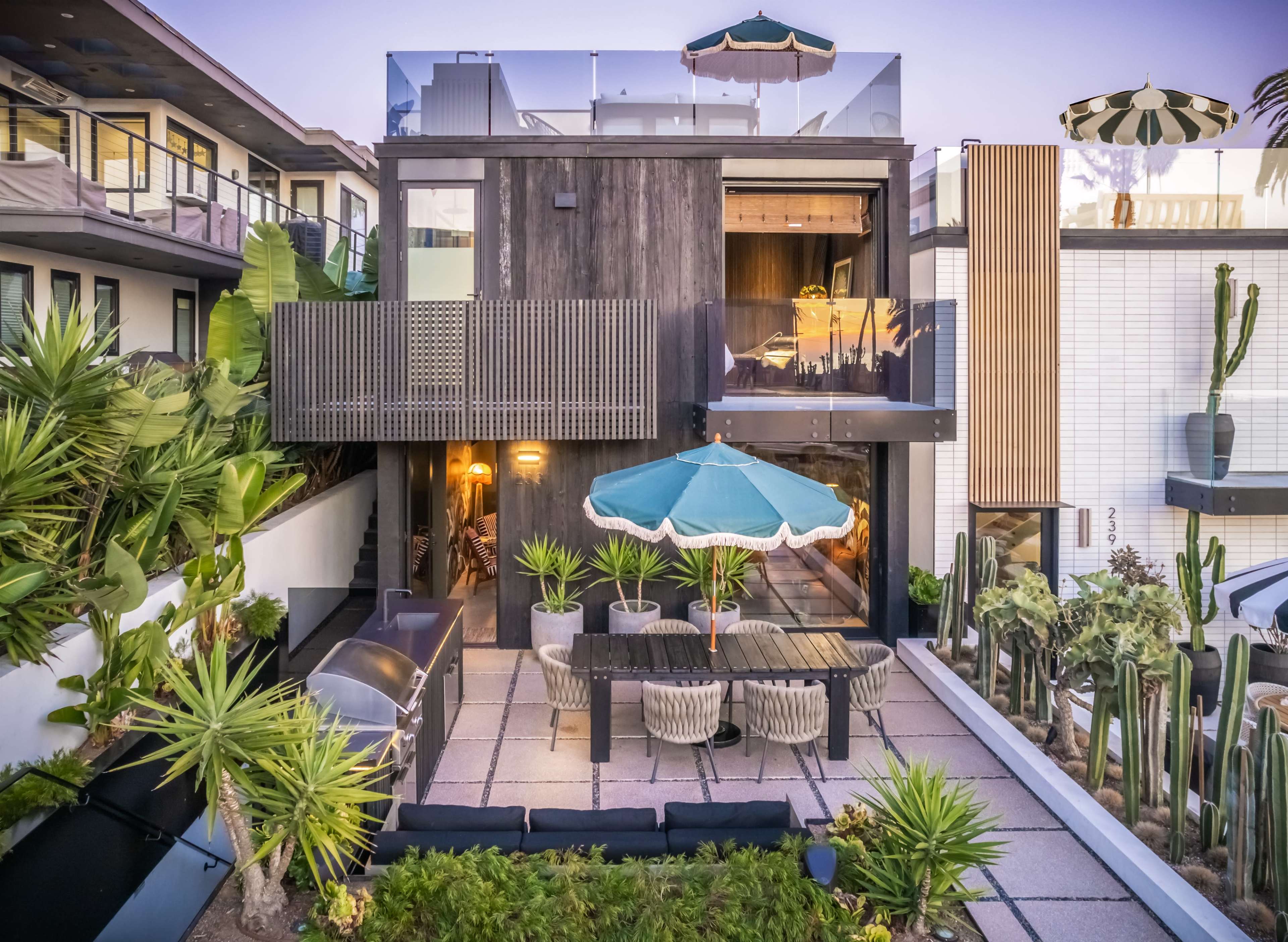 A modern house with a rooftop terrace and a patio area surrounded by various plants and outdoor furniture.