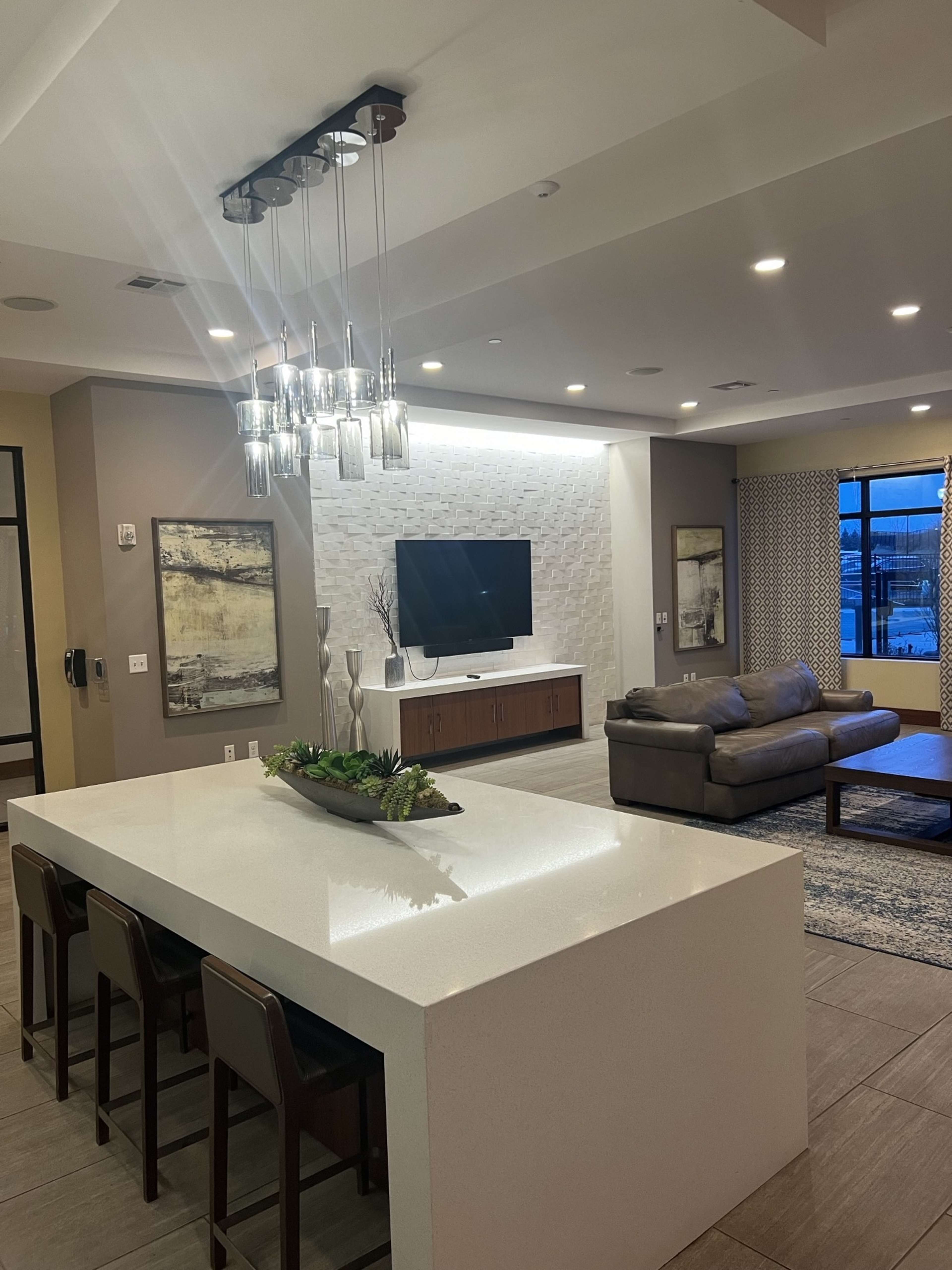 A modern living space with a white countertop island, a television mounted on the wall, and a gray sofa set in a well-lit room.