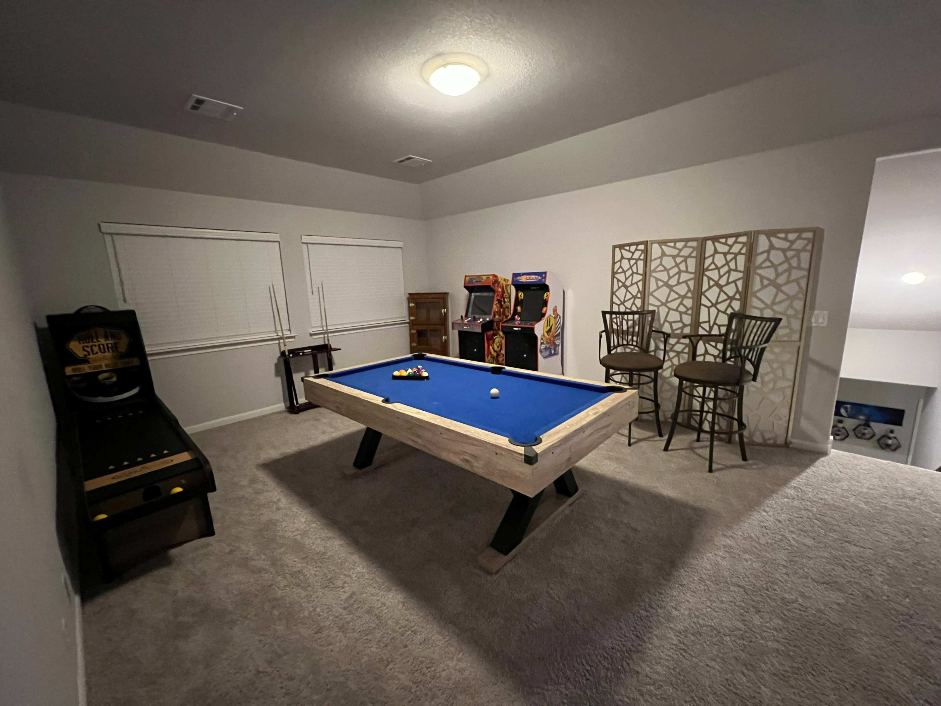 A game room with a pool table, arcade machines, bar stools, and a decorative screen.