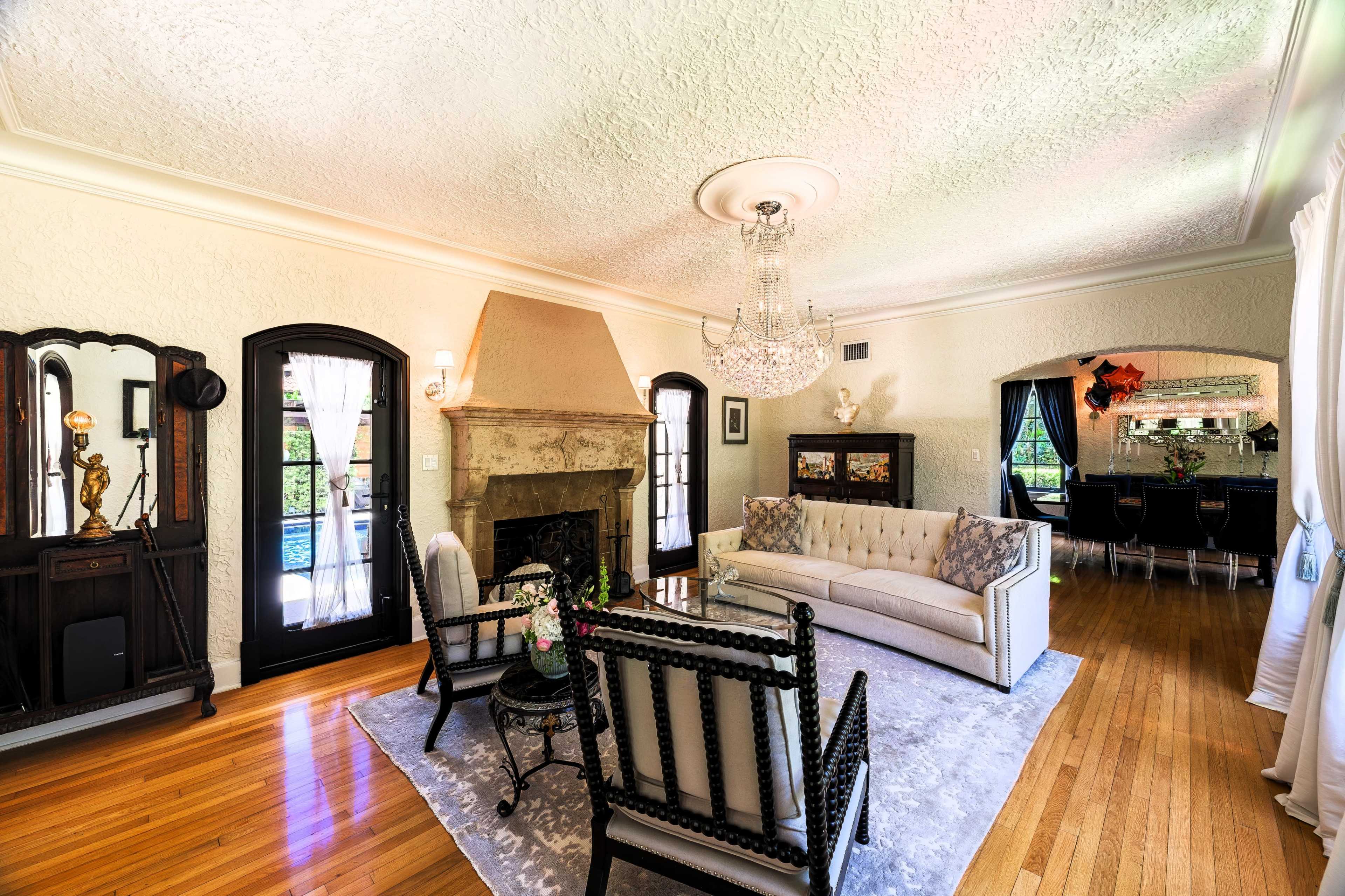 The room features a cozy living area with a fireplace, a chandelier, and elegant furniture arranged around a central area rug.