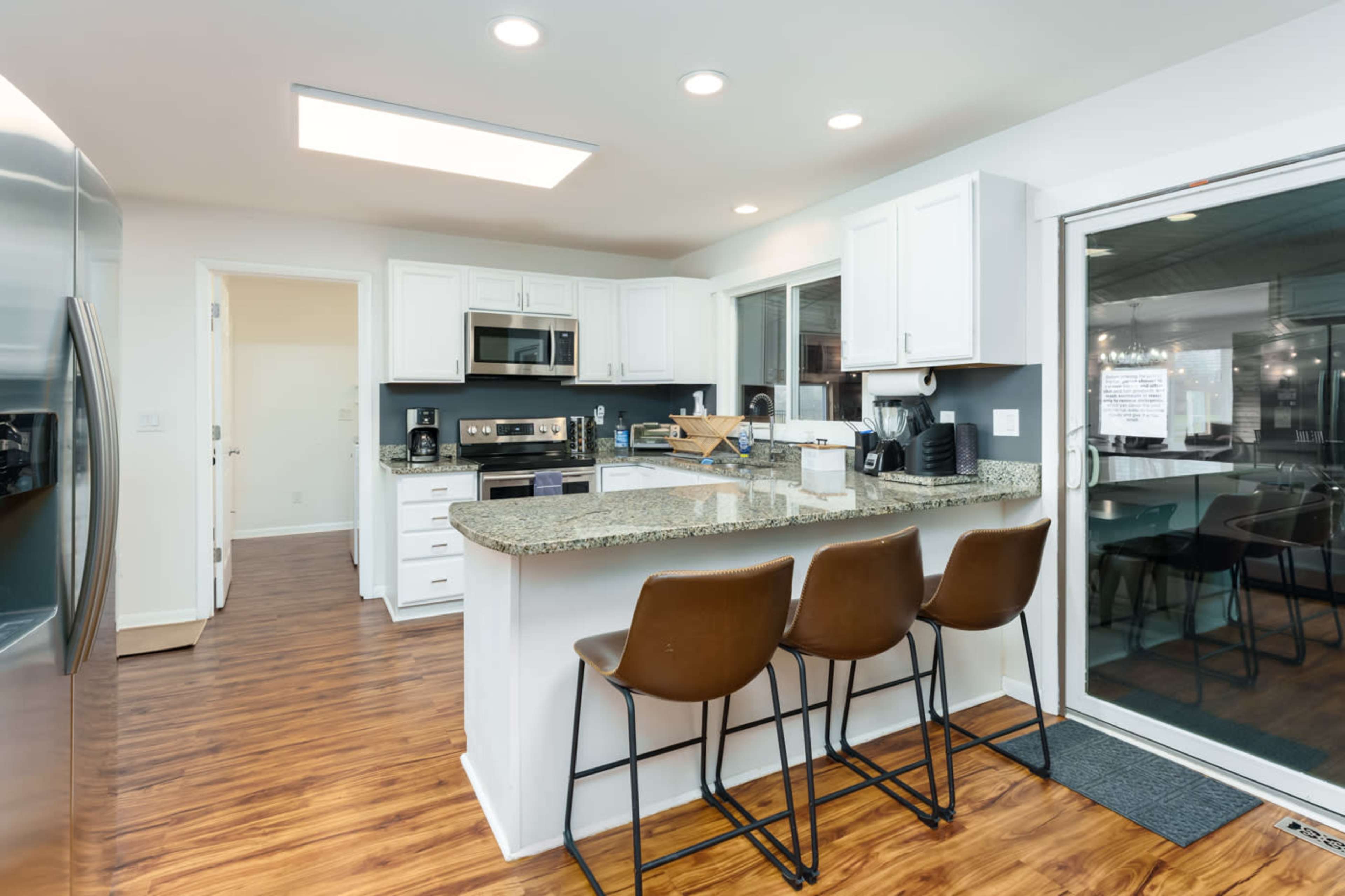 A modern kitchen features white cabinetry, stainless steel appliances, and a central island with seating for three.