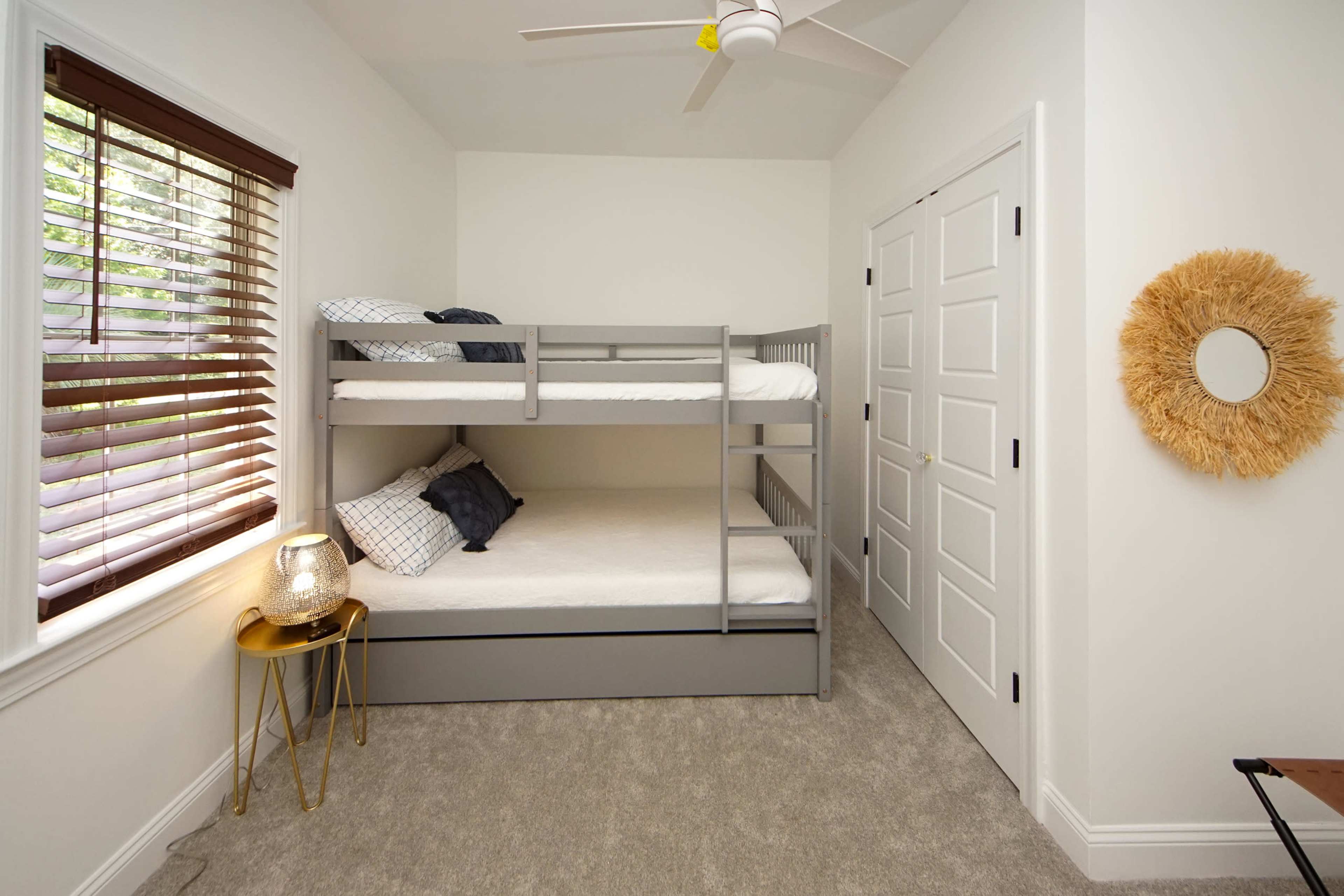 A small bedroom with a gray bunk bed, a round mirror on the wall, a lamp on a side table, and a closet door.