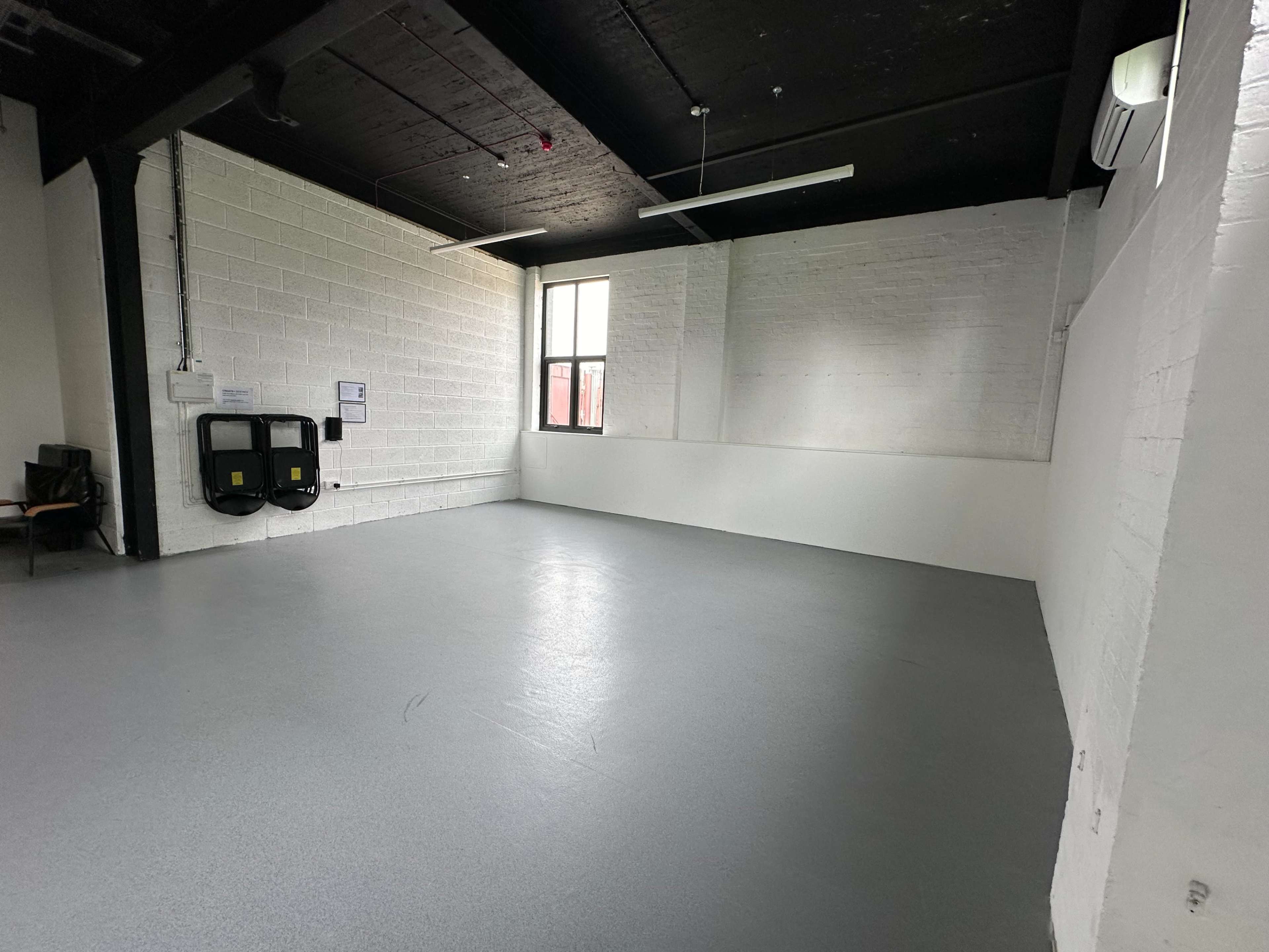 An empty room with gray flooring, white walls, and a window, along with two wall-mounted fixtures.