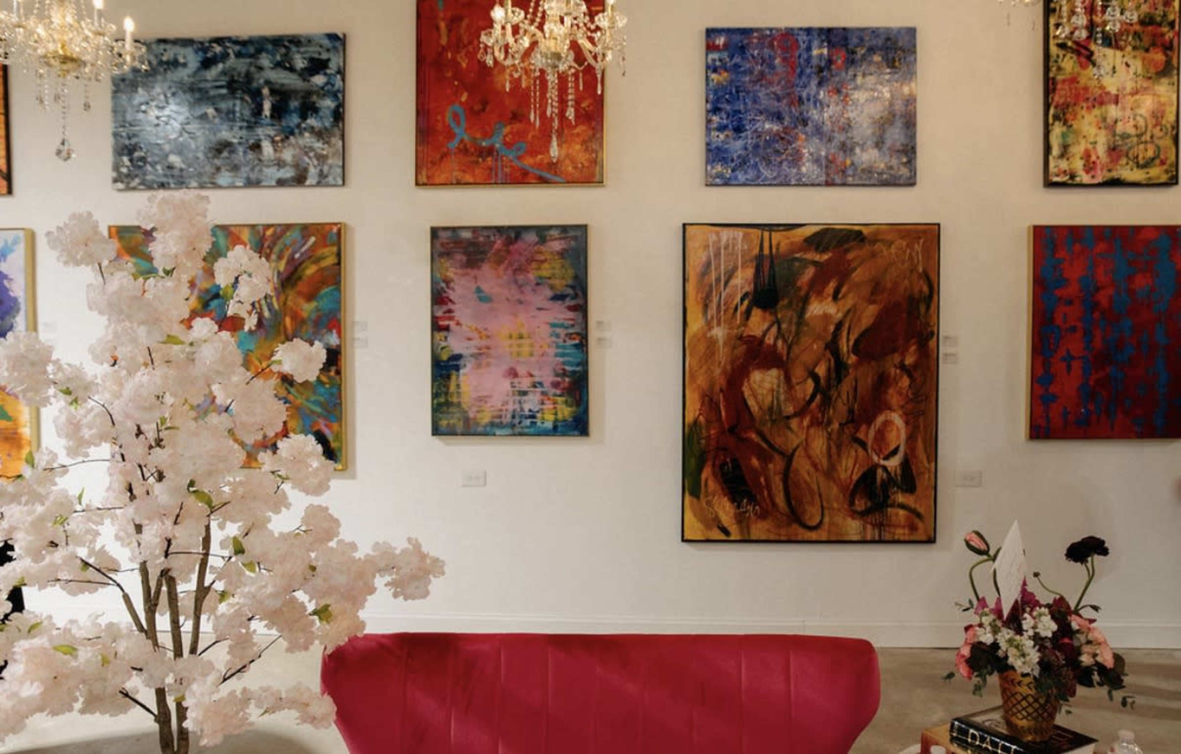 The scene features a bright art gallery with colorful abstract paintings on the walls and a pink couch in the center, accompanied by decorative flowers and a chandelier.