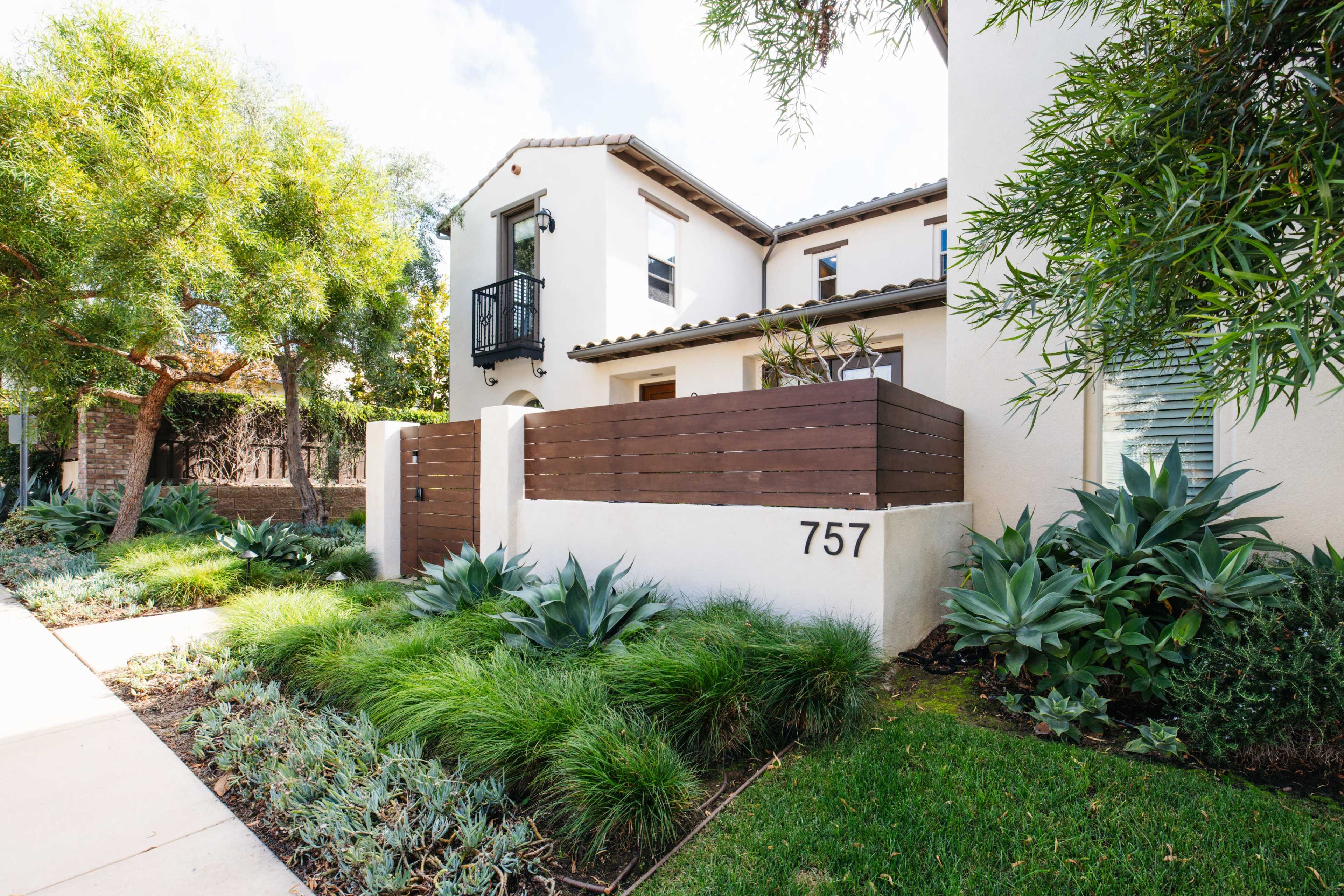 A residential property with a wooden fence bearing the number 757, surrounded by landscaped greenery and plants.