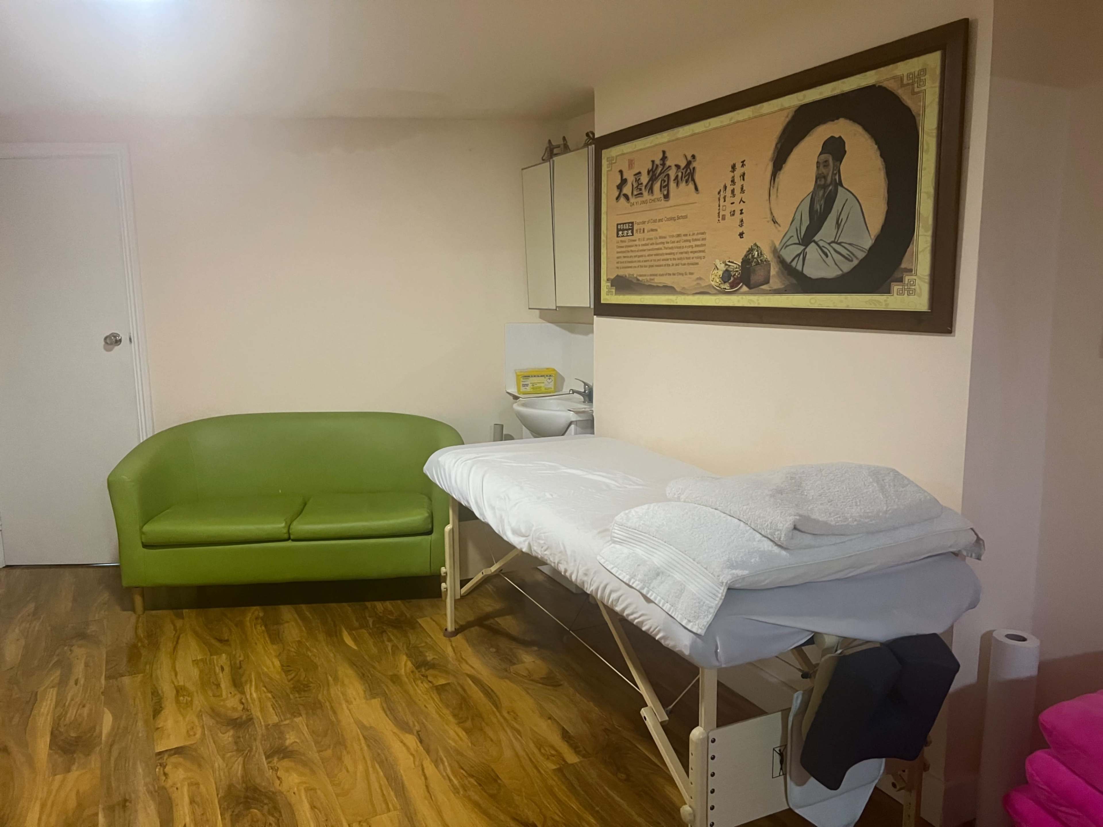 The room features a green sofa, a massage table with white linens, and a large framed artwork on the wall.