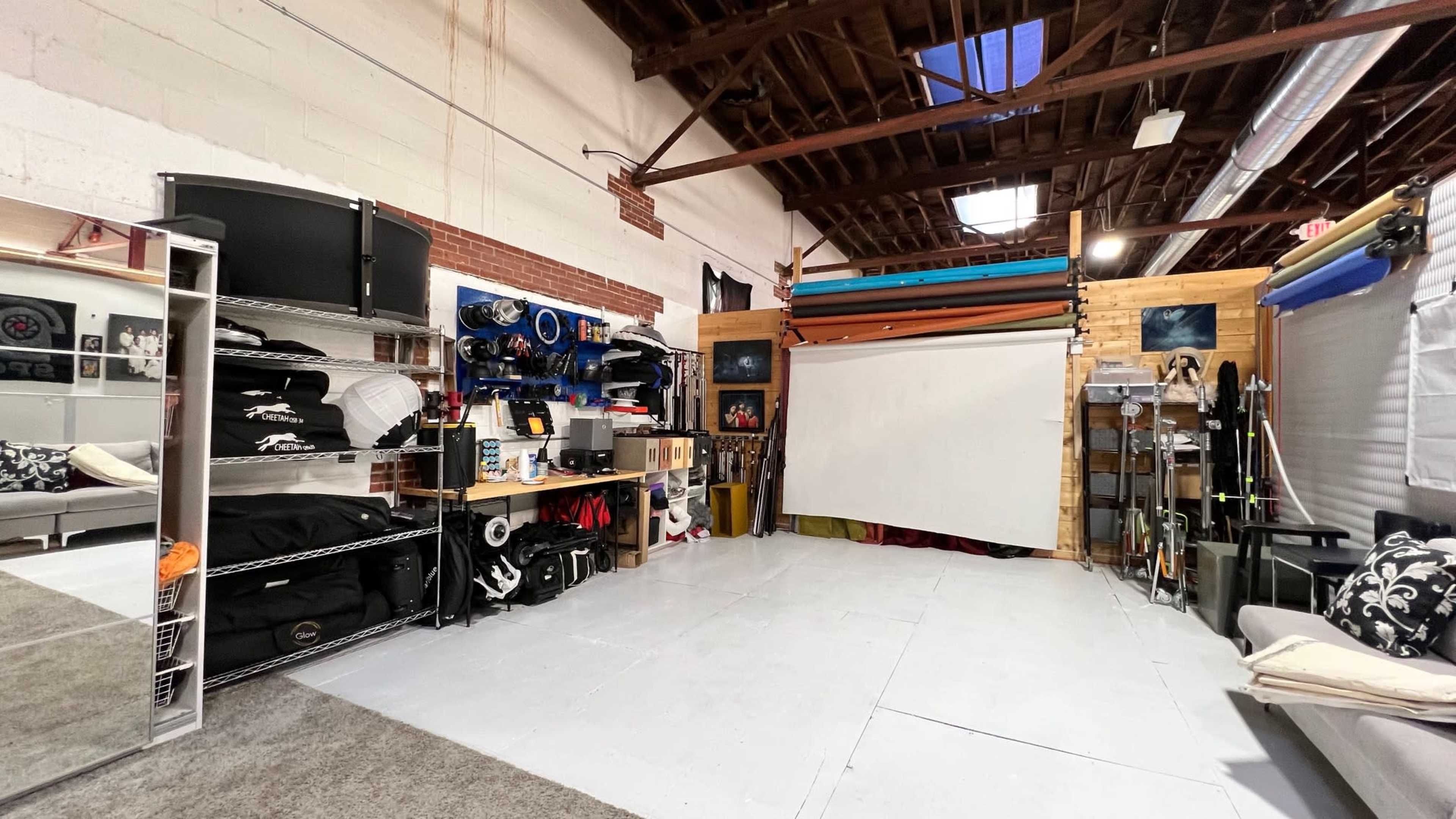 The image shows an organized workspace featuring shelves with equipment and materials, a blank projection screen, and a carpeted floor.