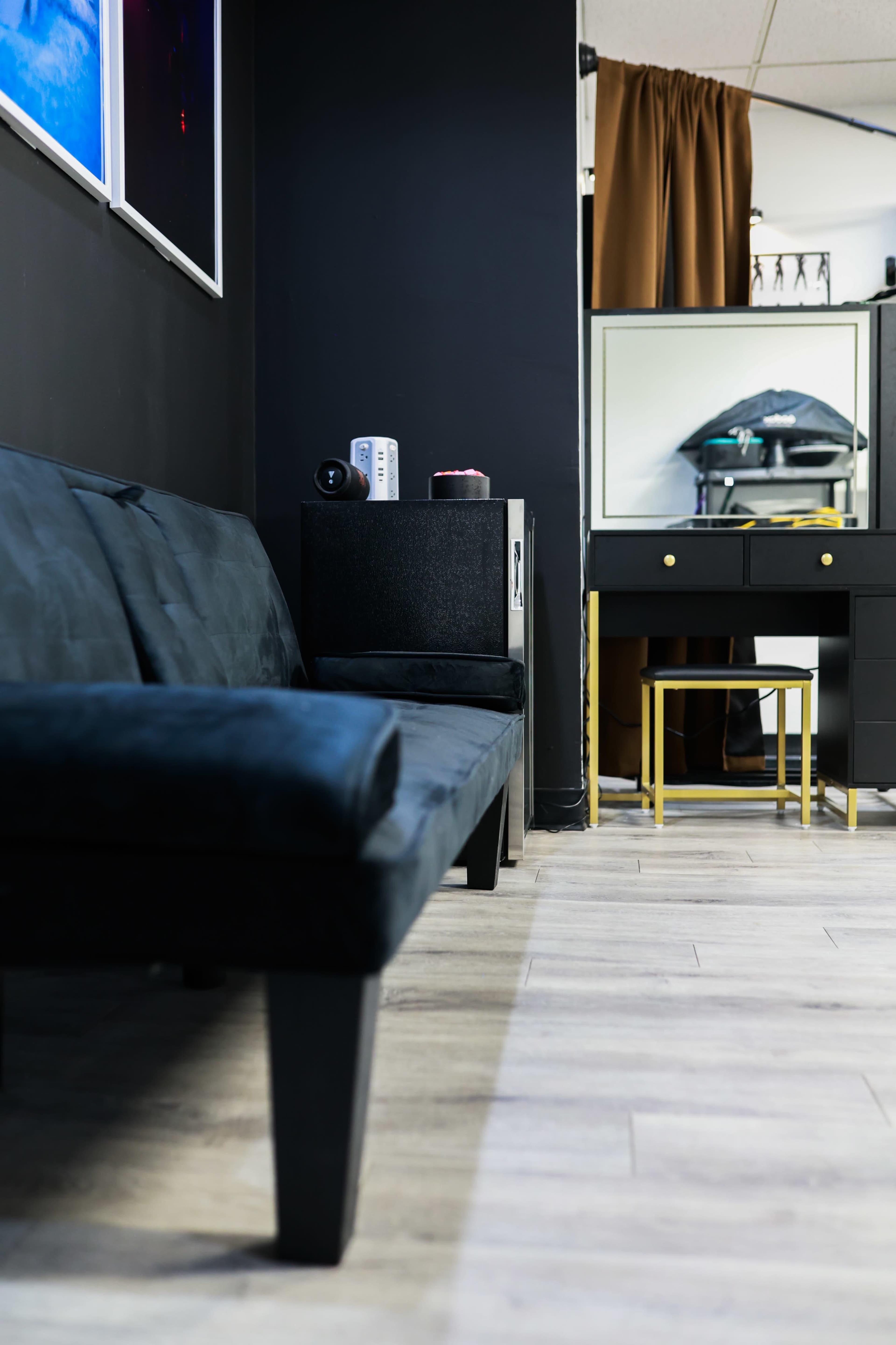 The image shows a modern interior space with a black sofa, a mirrored vanity, and a curtain partially drawn in the background.
