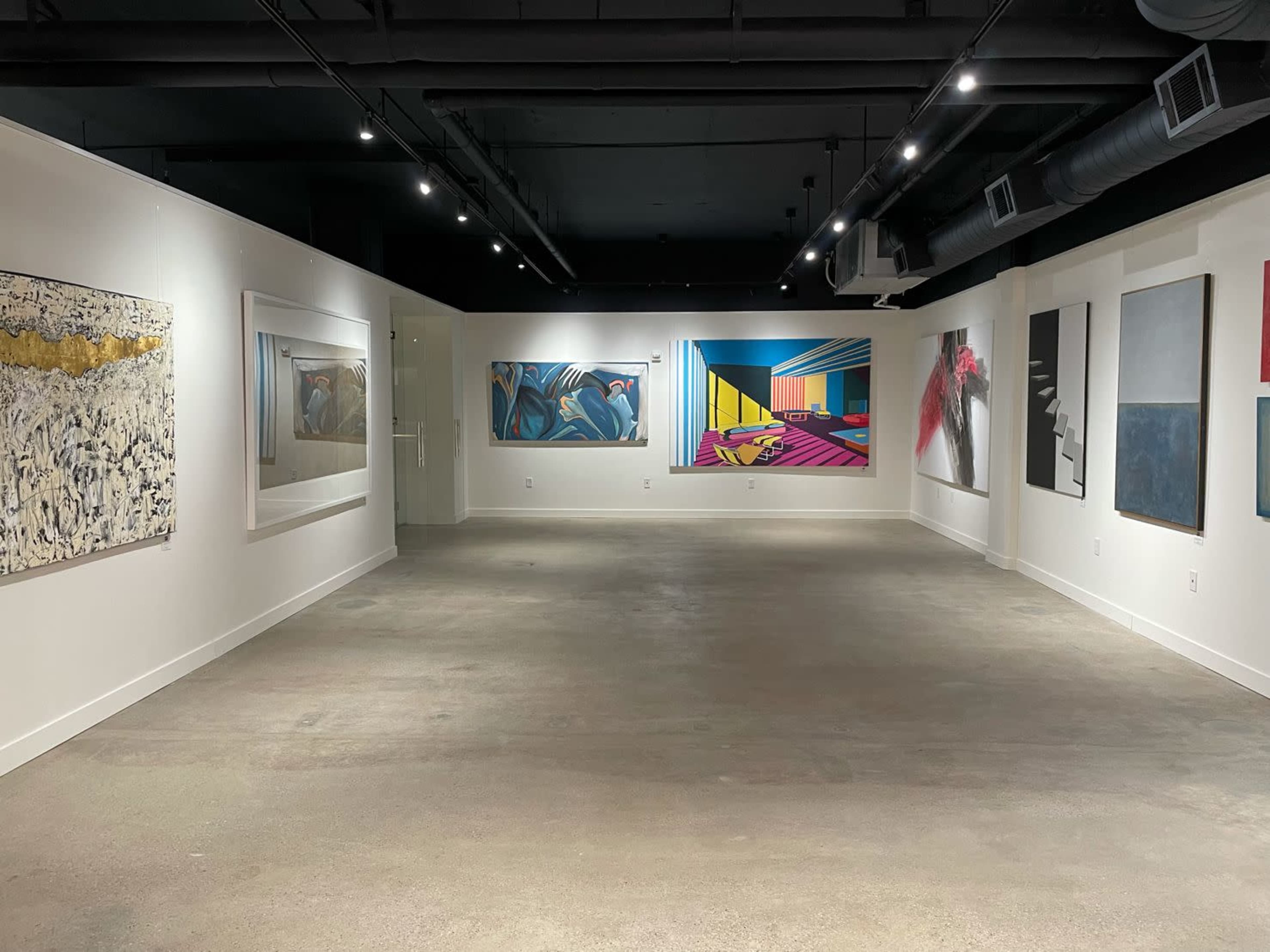 An art gallery with white walls displaying various artworks, illuminated by overhead track lighting.