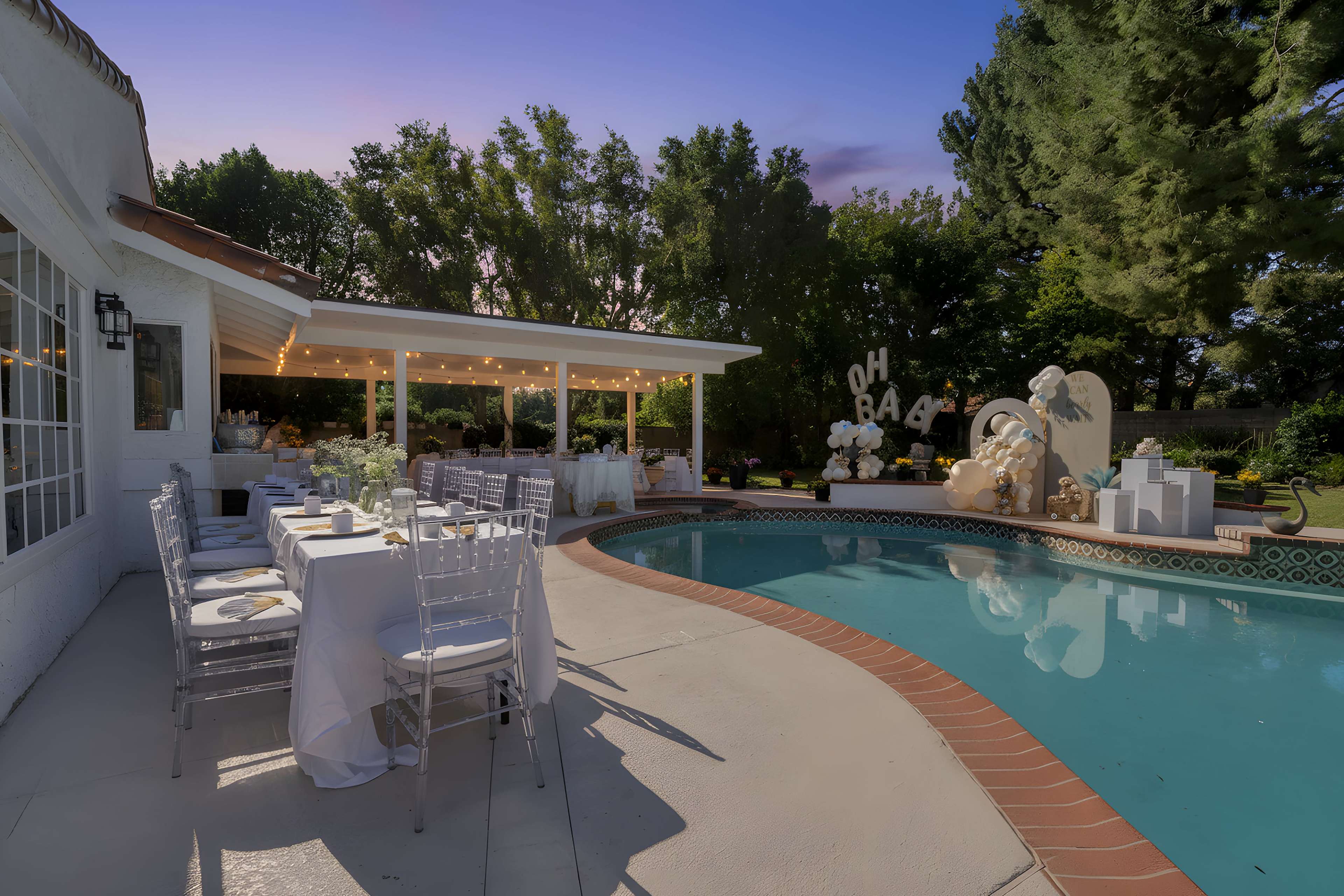 A backyard setting features a sparkling pool surrounded by elegant tables and decorations for a celebration, with greenery and string lights enhancing the ambiance.