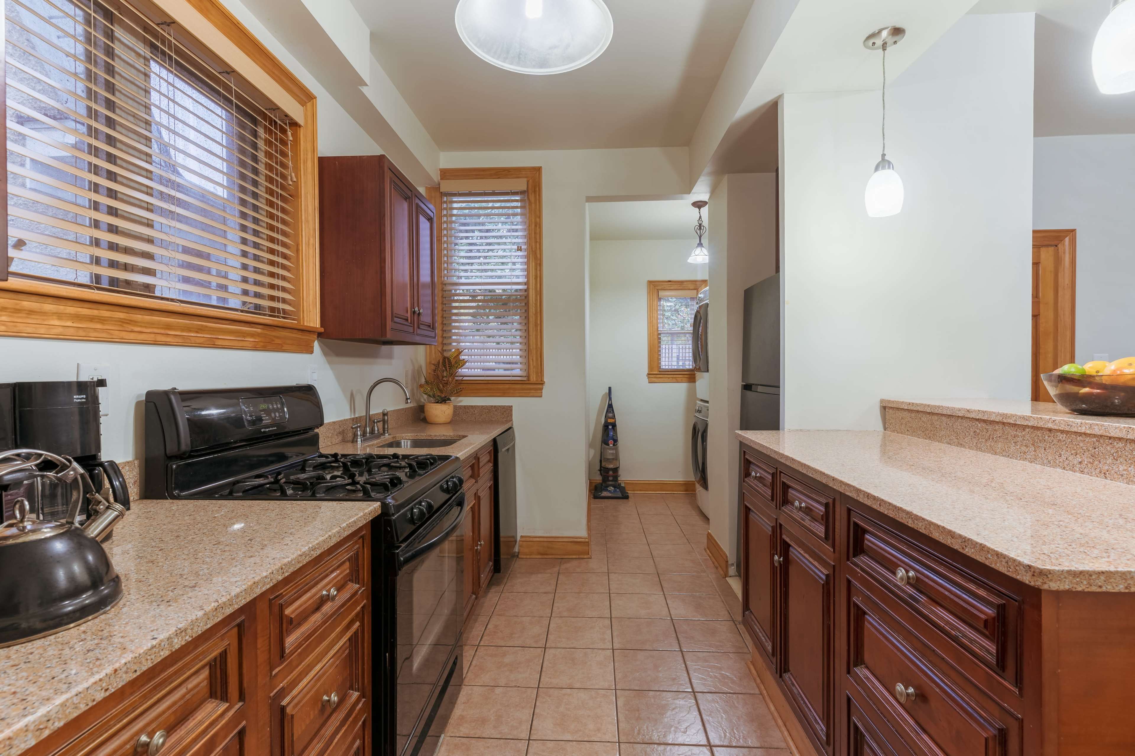 The image shows a kitchen featuring dark wood cabinetry, granite countertops, and stainless steel appliances, with a view toward a hallway at the back.