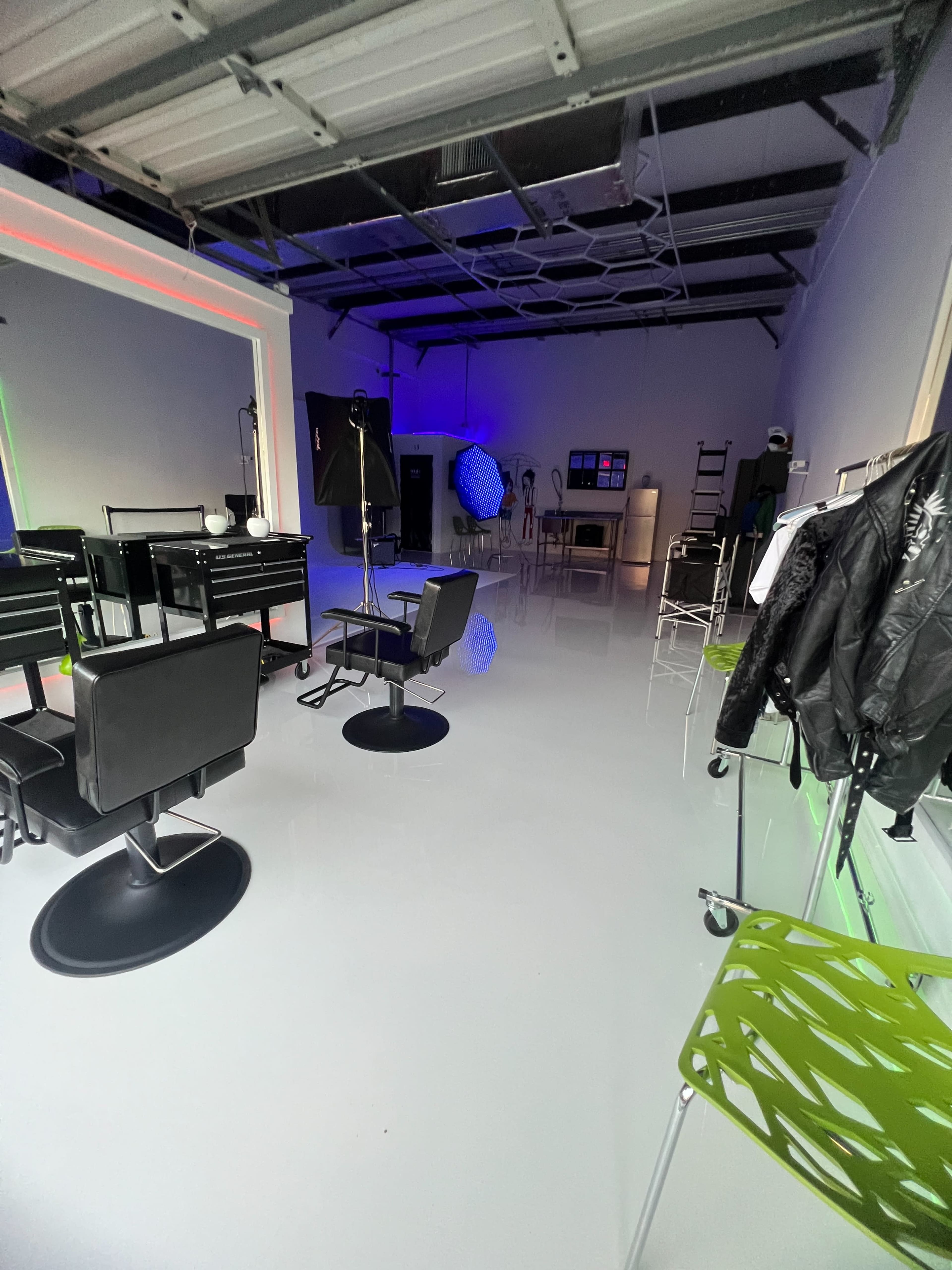 A spacious studio with black styling chairs, a green chair, and various equipment against walls featuring colored lighting.