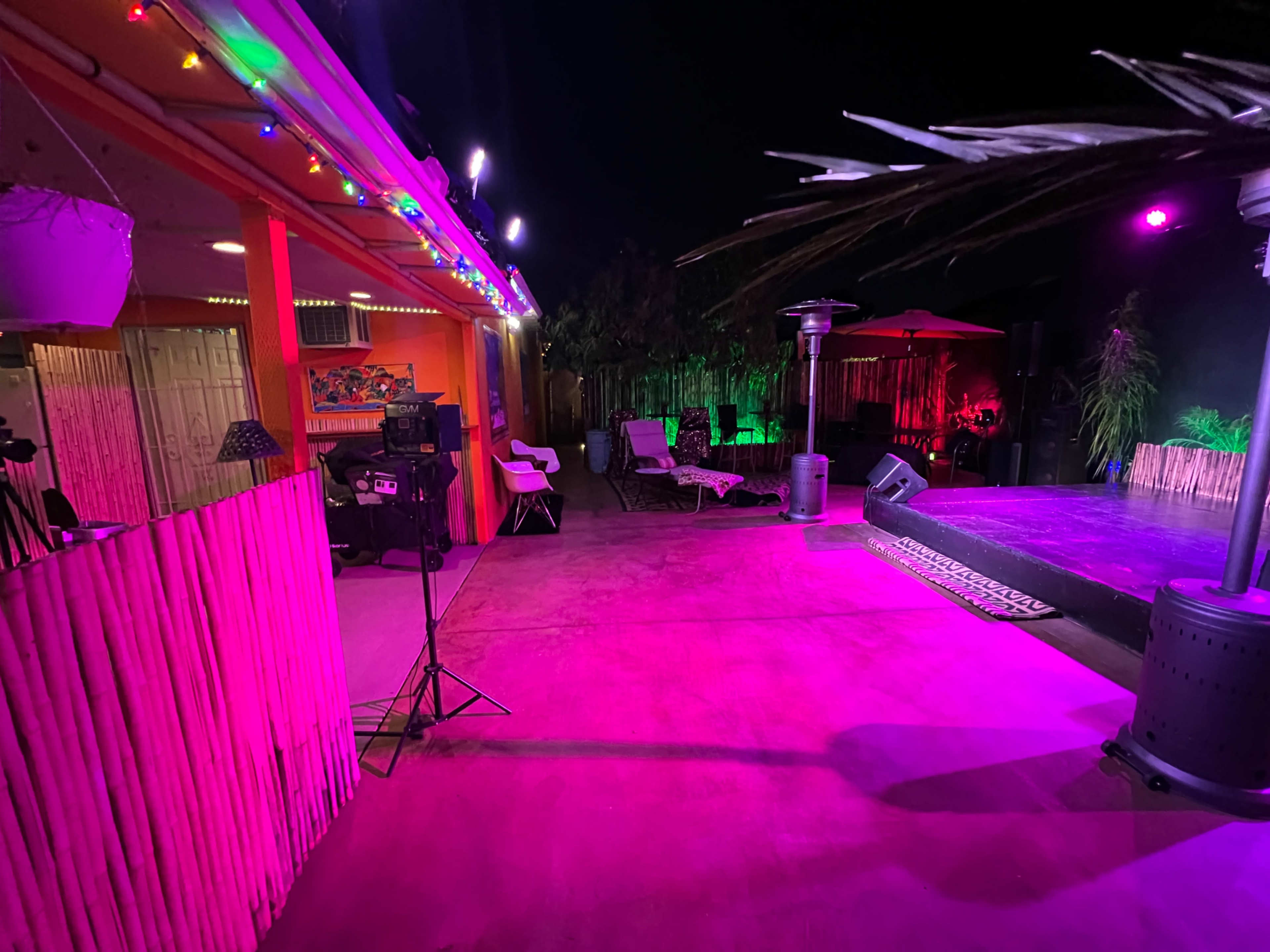 The scene features an outdoor space with colorful lighting, a stage area, seating, and equipment set up for an event at night.