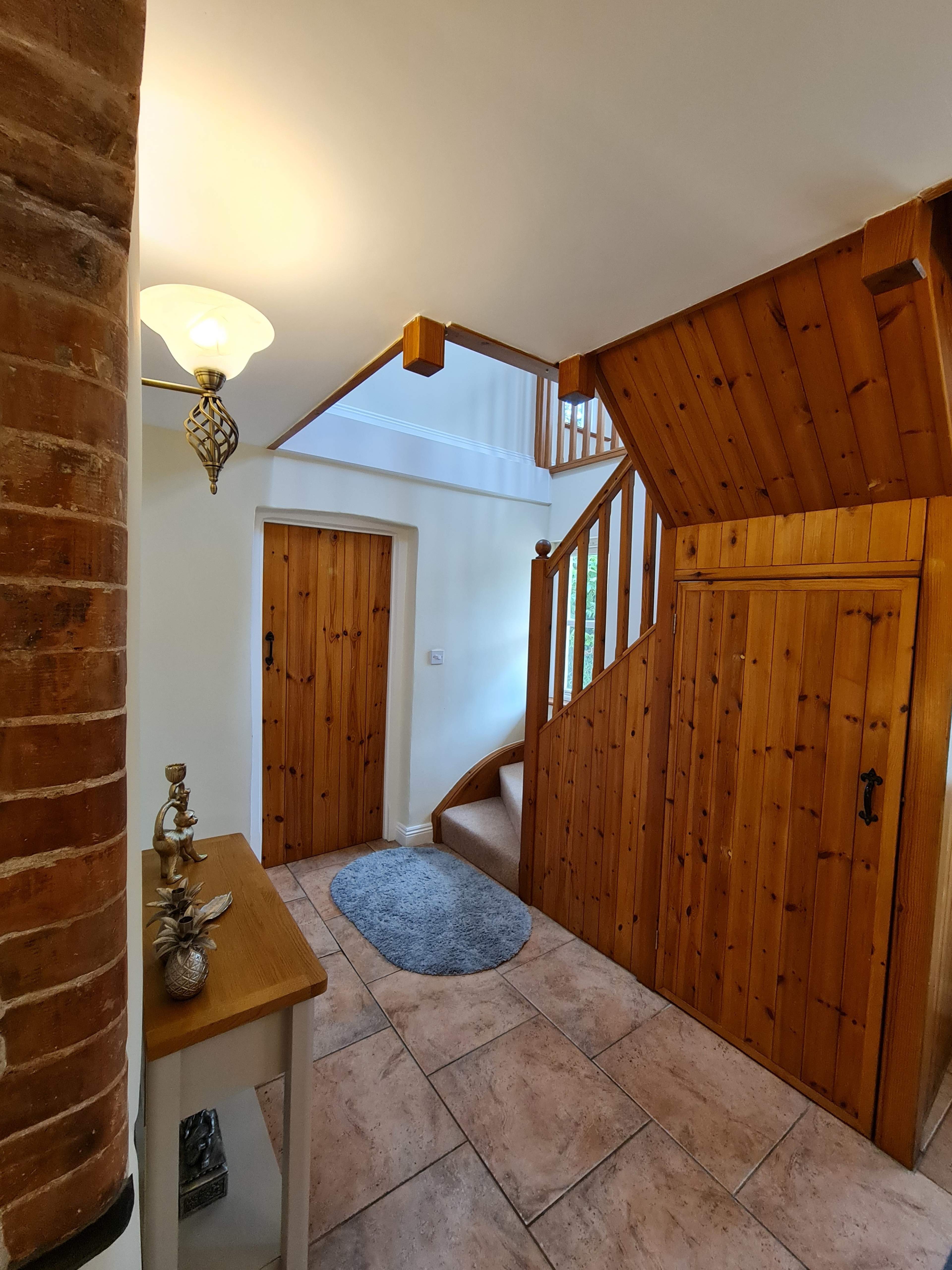 An entryway with a staircase, wooden doors, and a small table beside a round rug on tiled flooring.