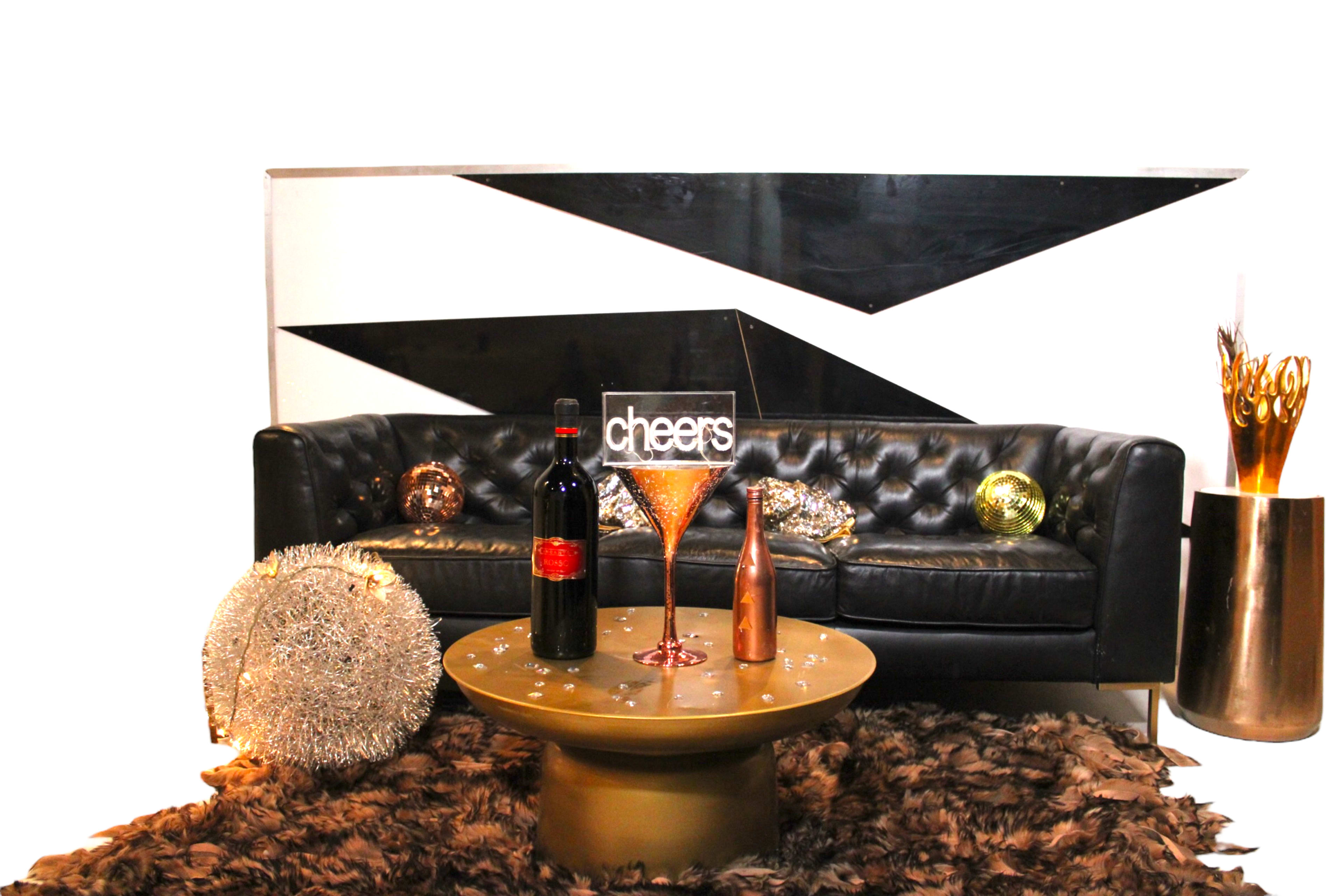 A black leather sofa is positioned against a geometric black and white wall, accompanied by a round coffee table adorned with a bottle of wine, a cocktail glass, and decorative objects.