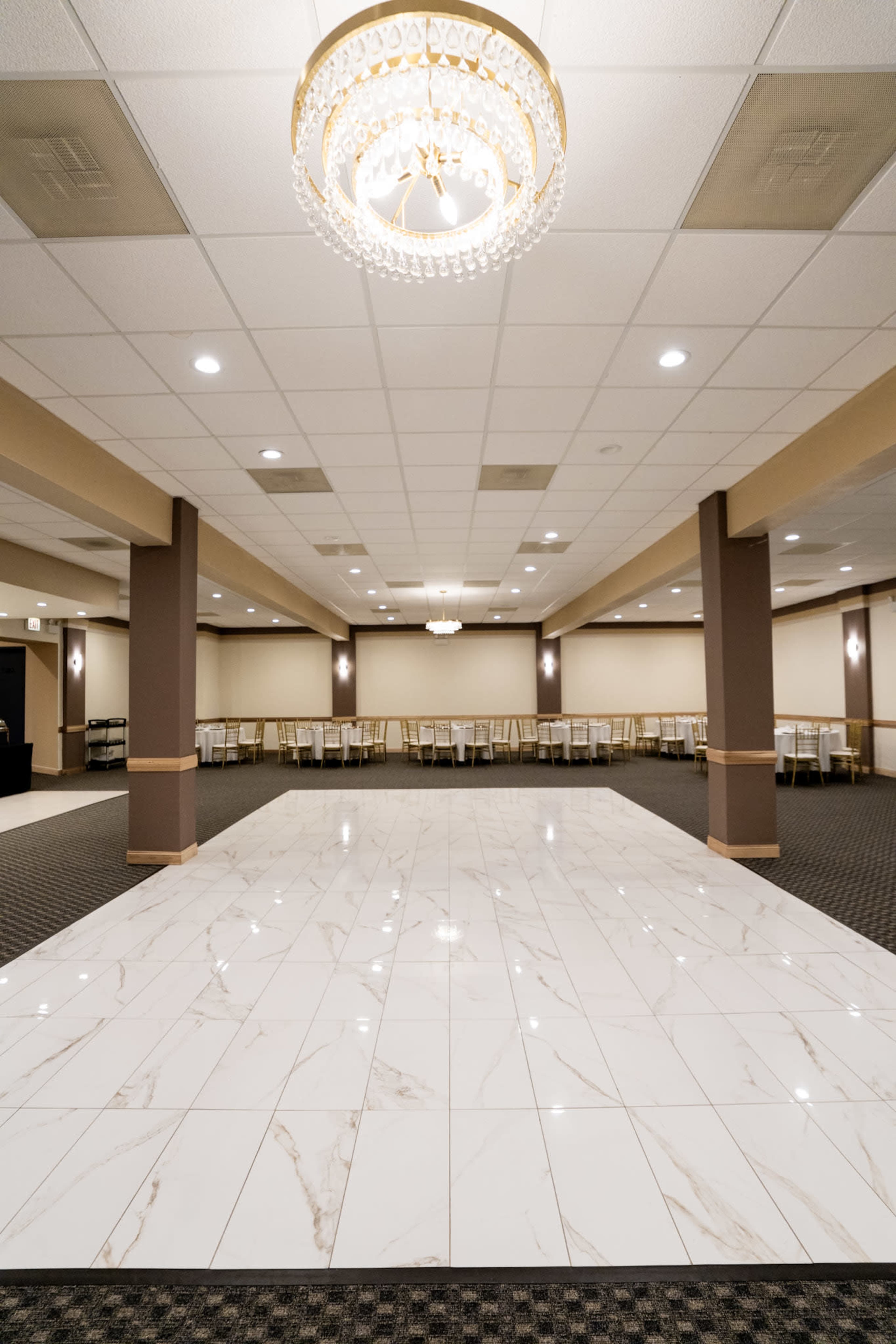 The image shows a spacious indoor venue with a glossy marble floor, elegant chandeliers, and rows of empty tables and chairs along the walls.