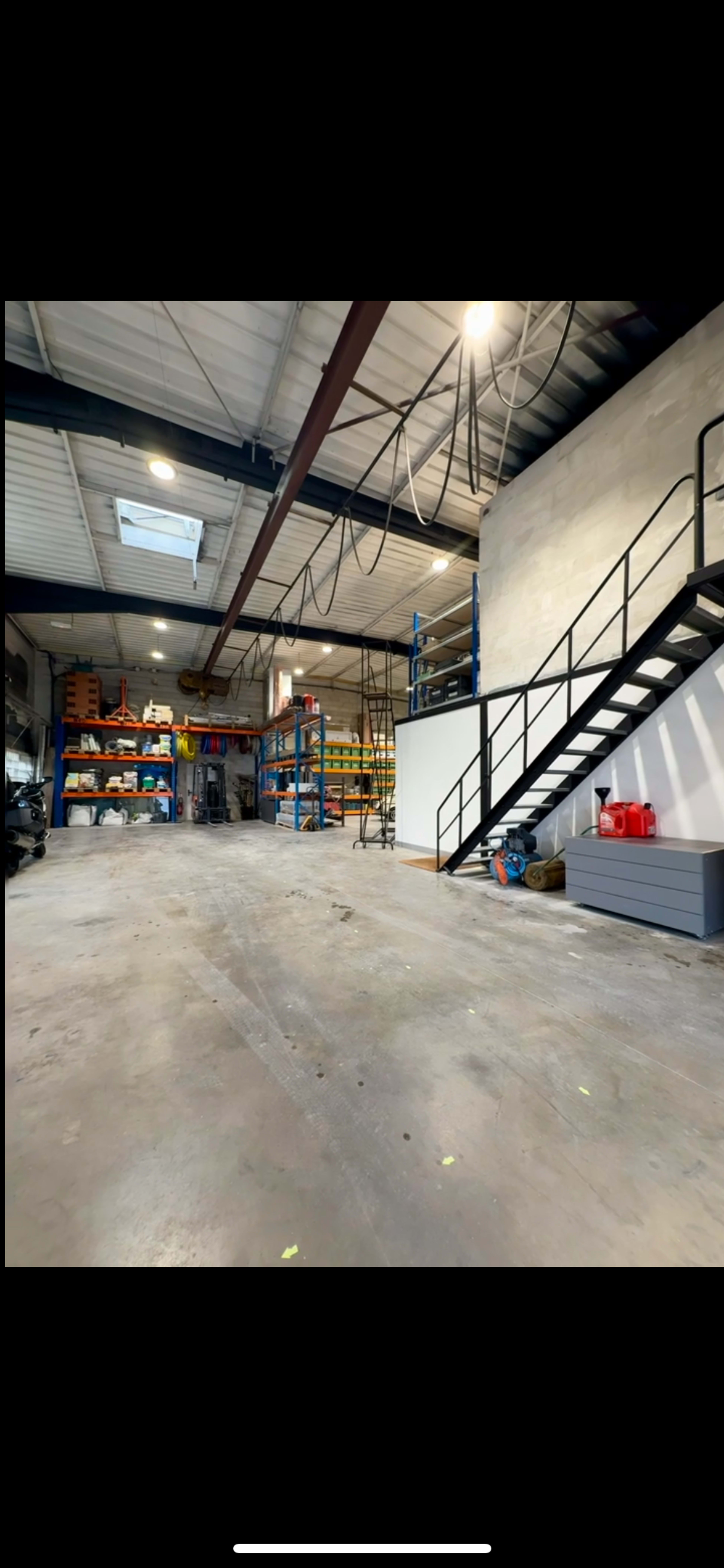 The image shows a spacious warehouse interior with shelving units, a staircase, and a concrete floor.
