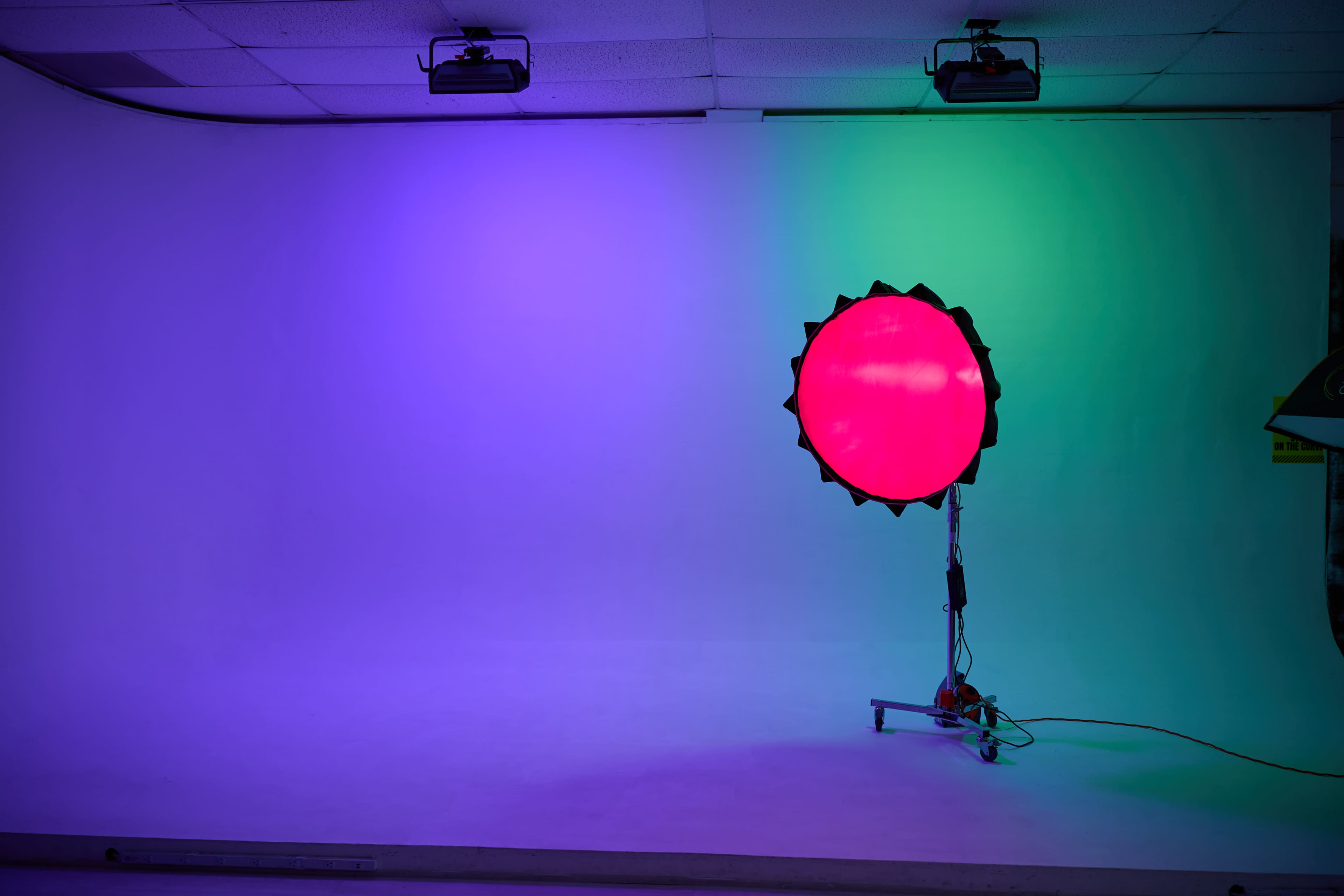 A large round light with a bright red center is positioned on a stand against a gradient backdrop of purple and green colors.