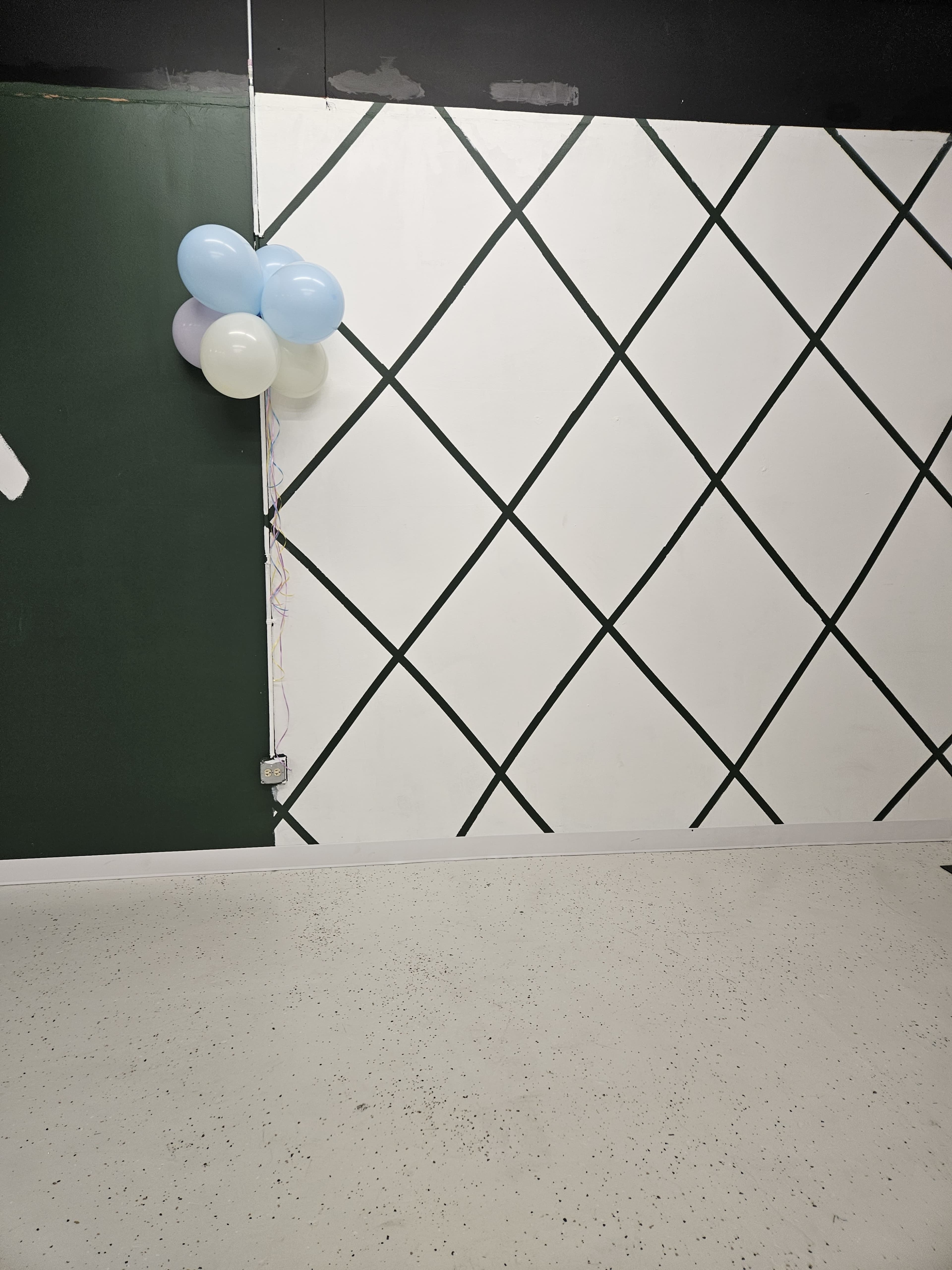 A corner of a room with a green wall, a white wall featuring a diamond pattern, and a cluster of balloons in blue and white.