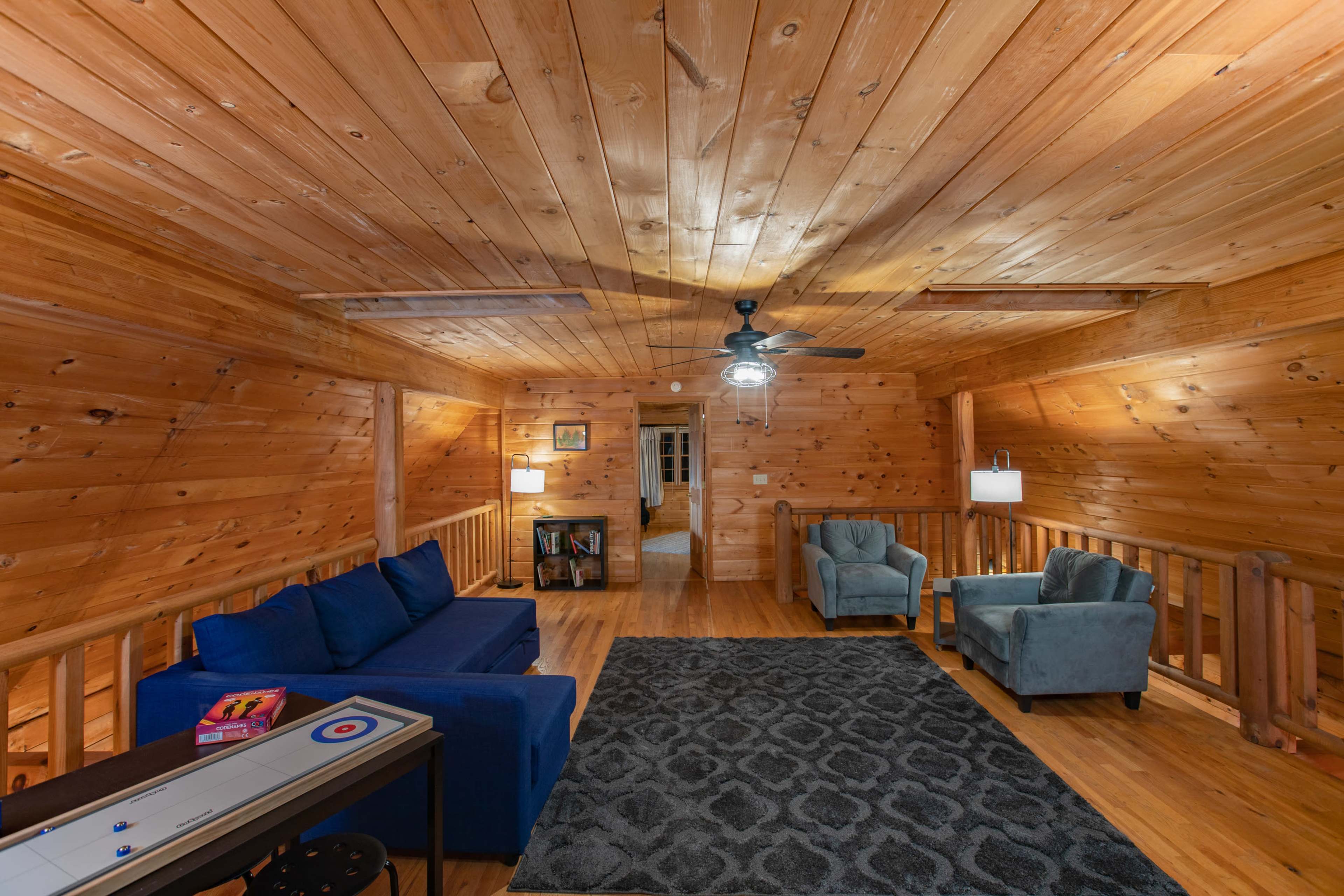 The room features wooden paneled walls and ceiling, with a blue sofa, two light blue chairs, and a patterned rug on the wooden floor.