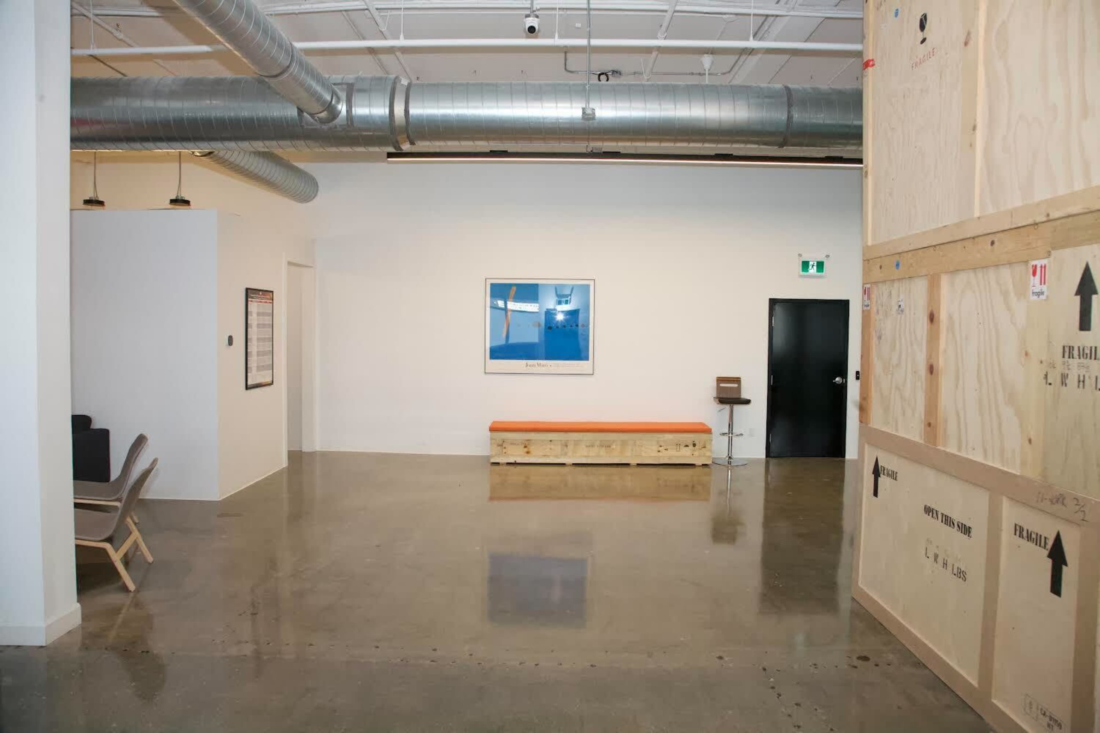 The image shows a minimalistic interior space featuring polished concrete flooring, a wooden bench along one wall, and a framed picture on another wall.