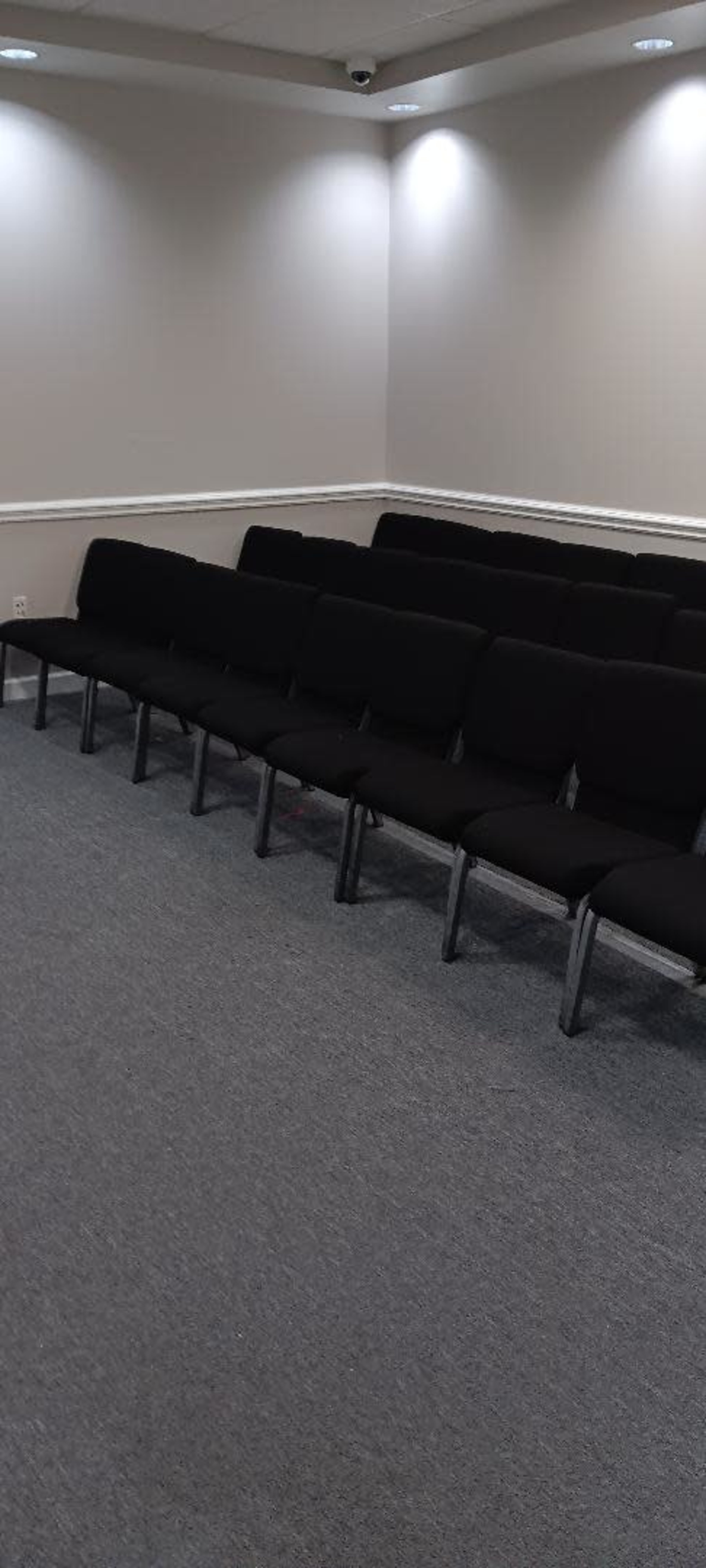 A row of black chairs arranged in an empty, well-lit meeting room with gray carpeting.