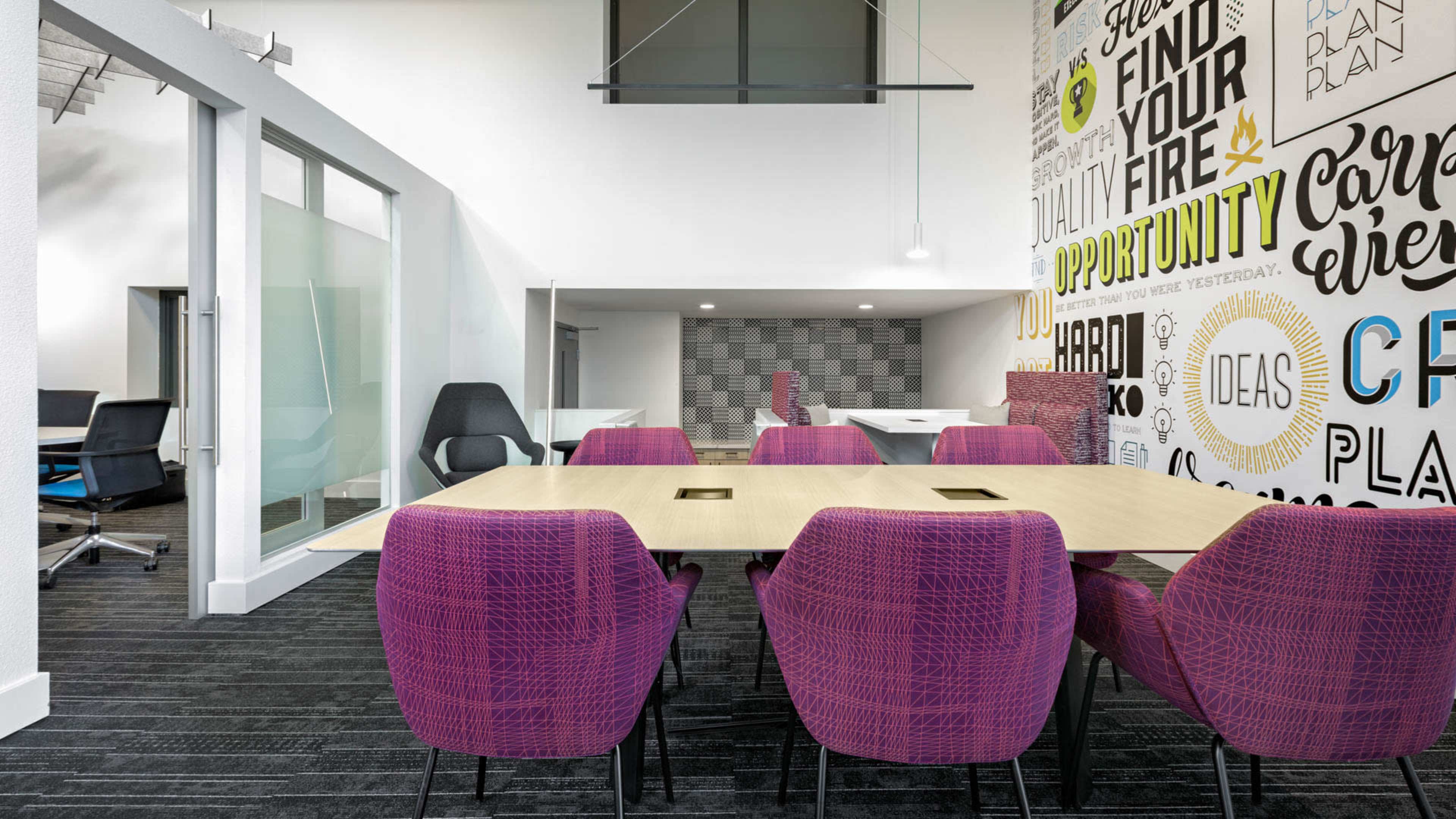The image shows a modern conference room with a large rectangular table surrounded by purple chairs, and a wall decorated with motivational phrases.