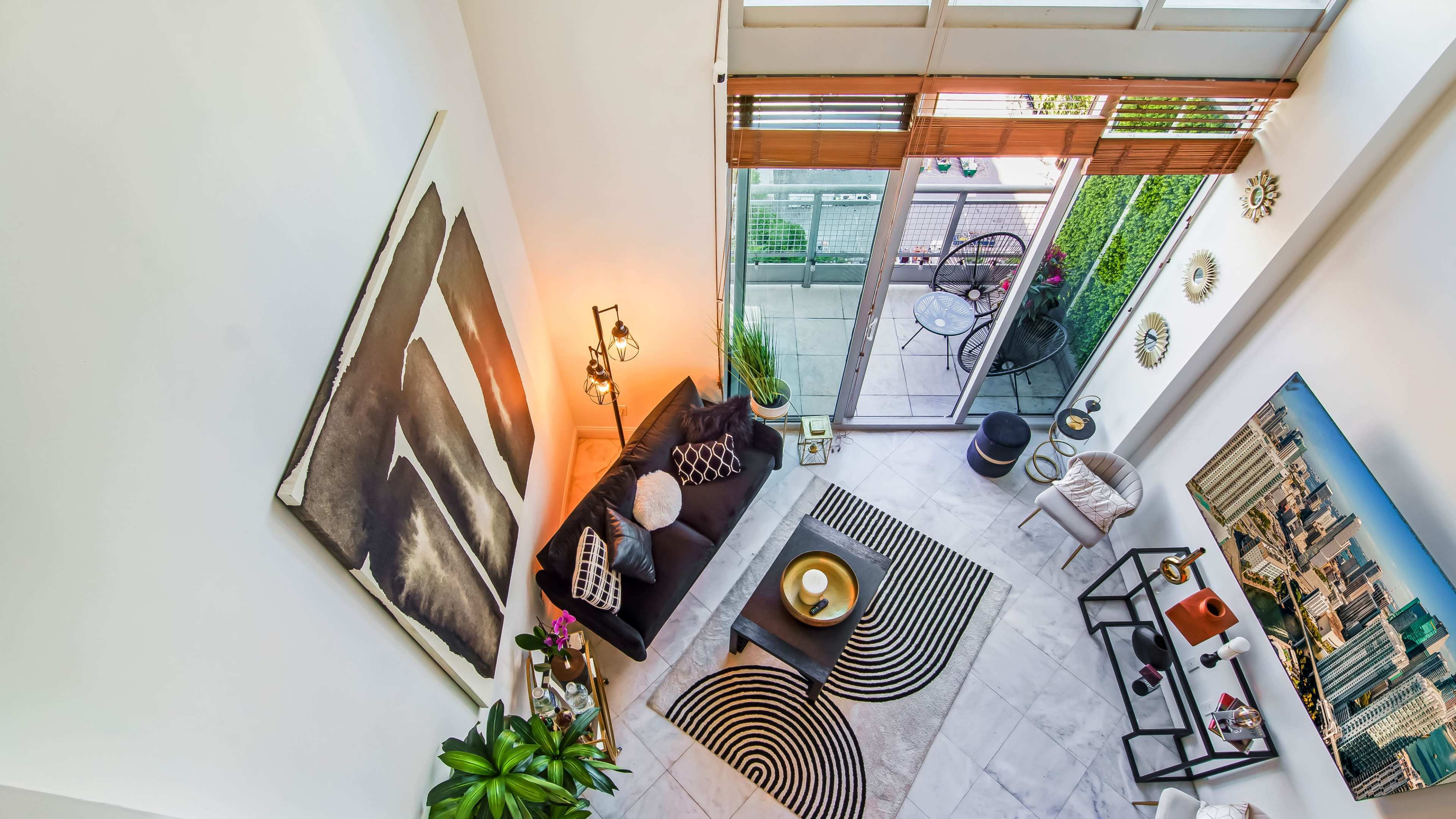 A modern living room with high ceilings, a black sofa, a circular coffee table, and large windows leading to a balcony.