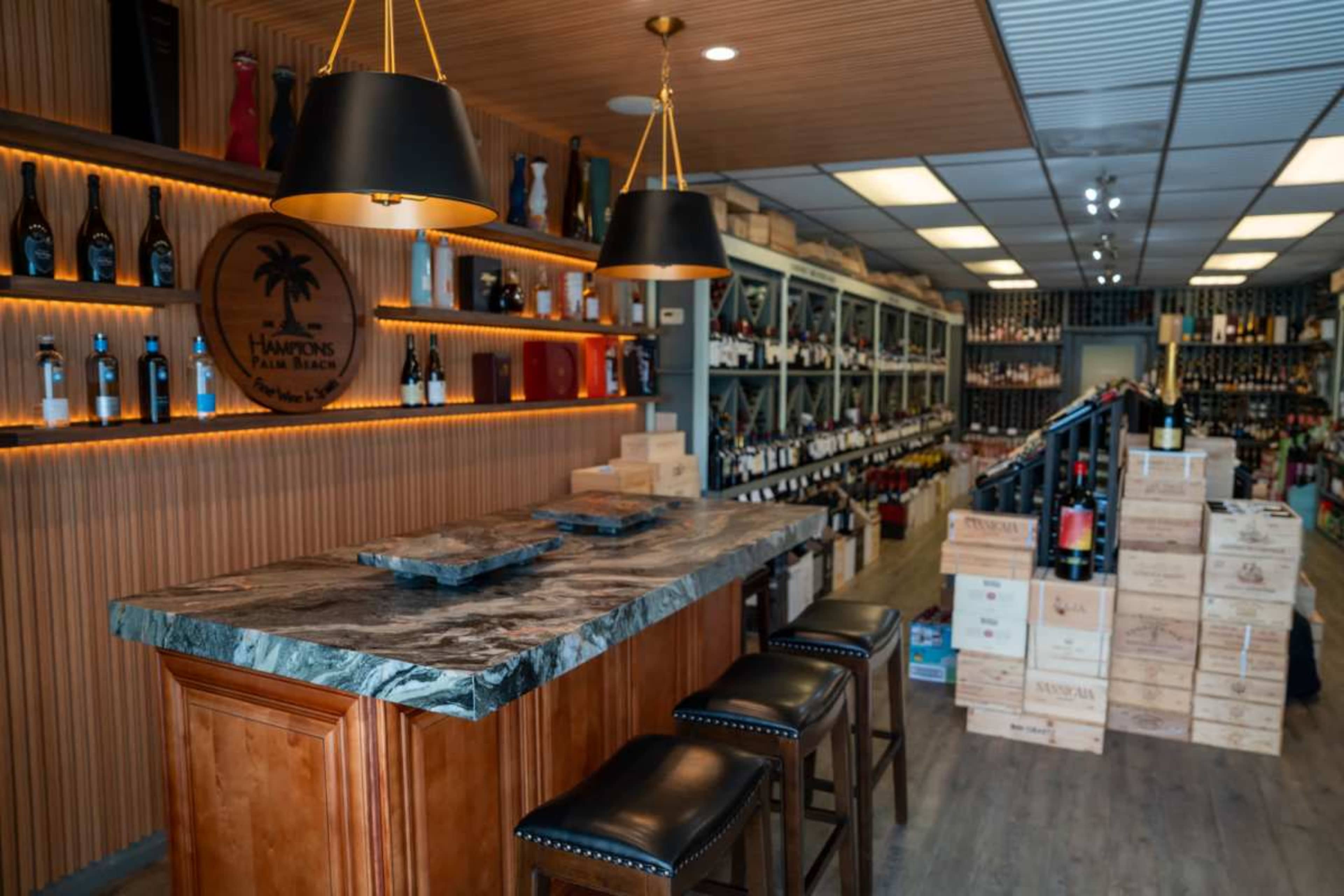 The interior of a wine shop features a wooden bar with black stools, surrounded by shelves stocked with various bottles of wine and decorative items.