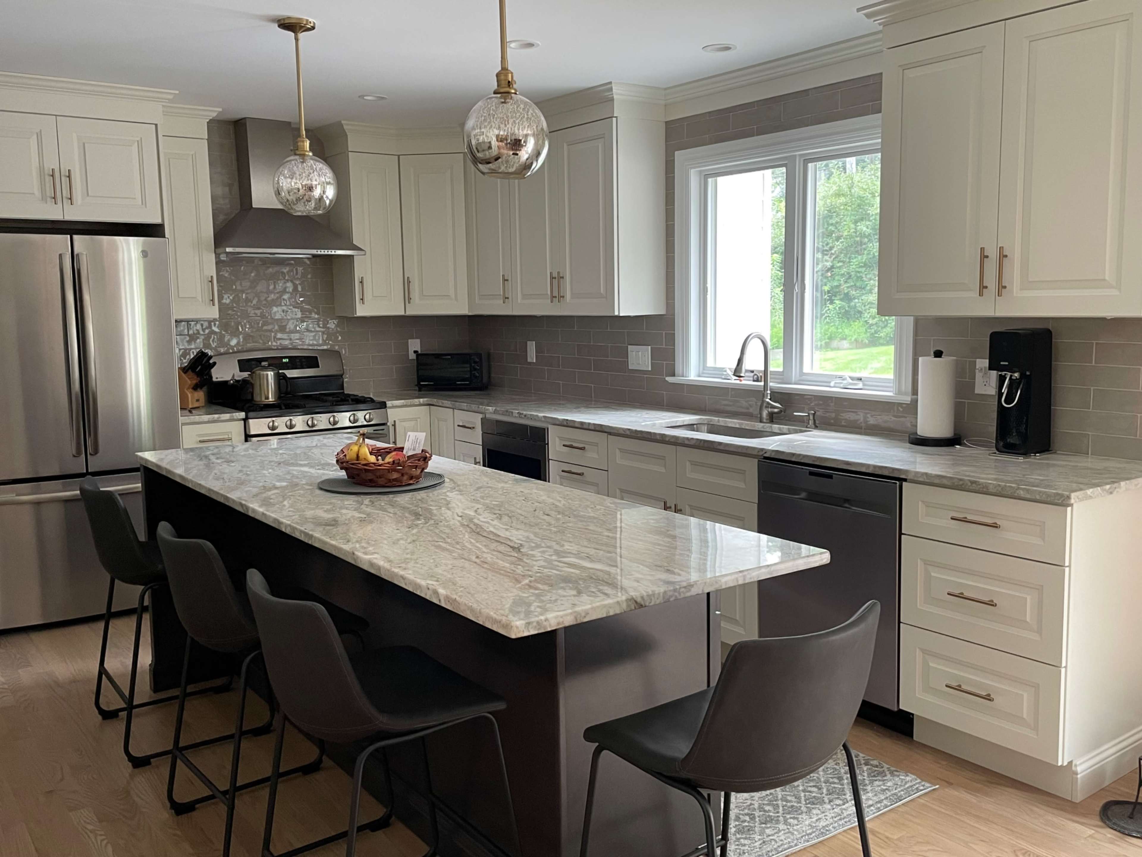 A modern kitchen with white cabinetry, stainless steel appliances, a large marble island, and bar seating.