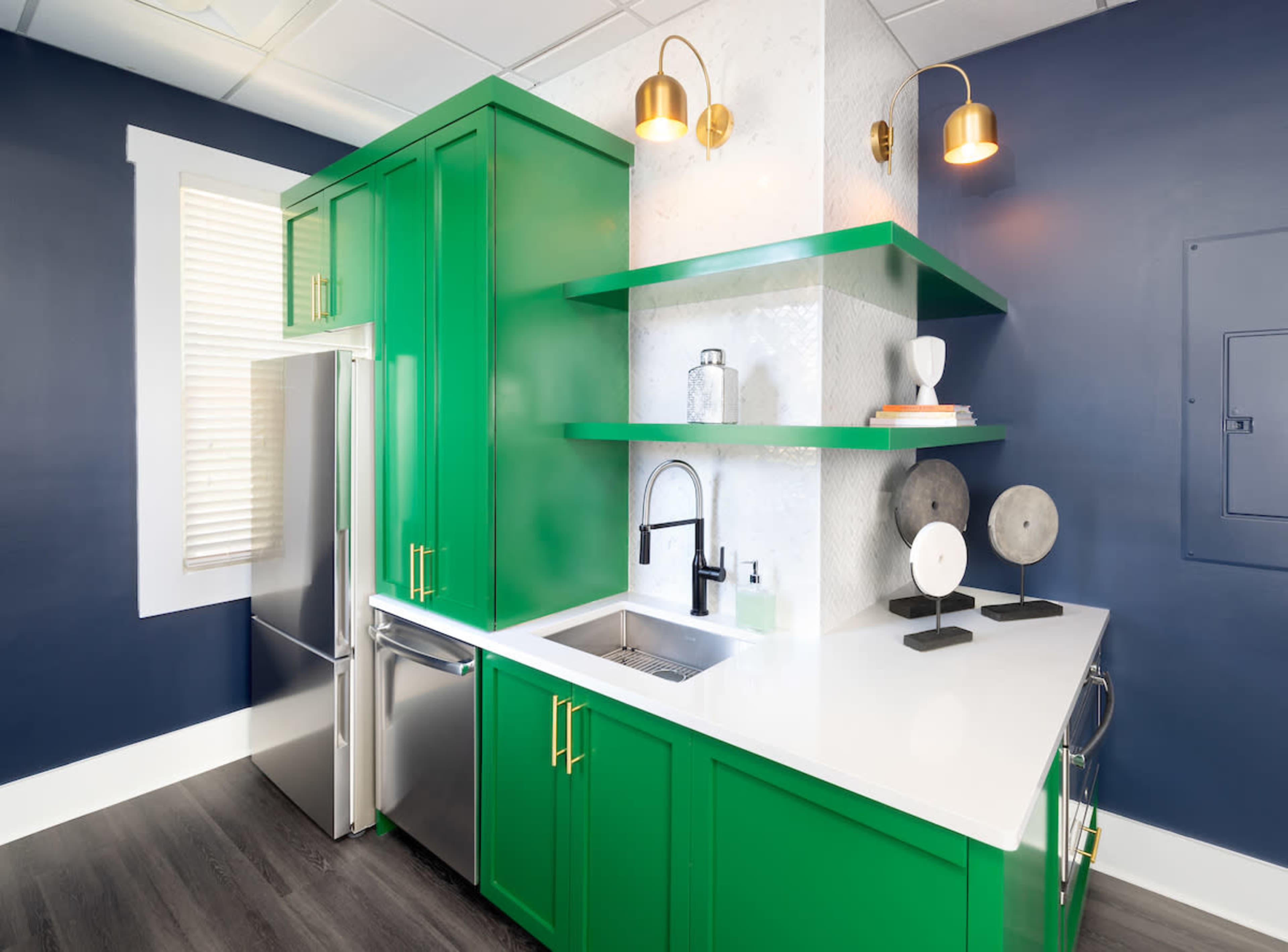 A kitchen with vibrant green cabinets, stainless steel appliances, and white countertops, set against a blue wall.