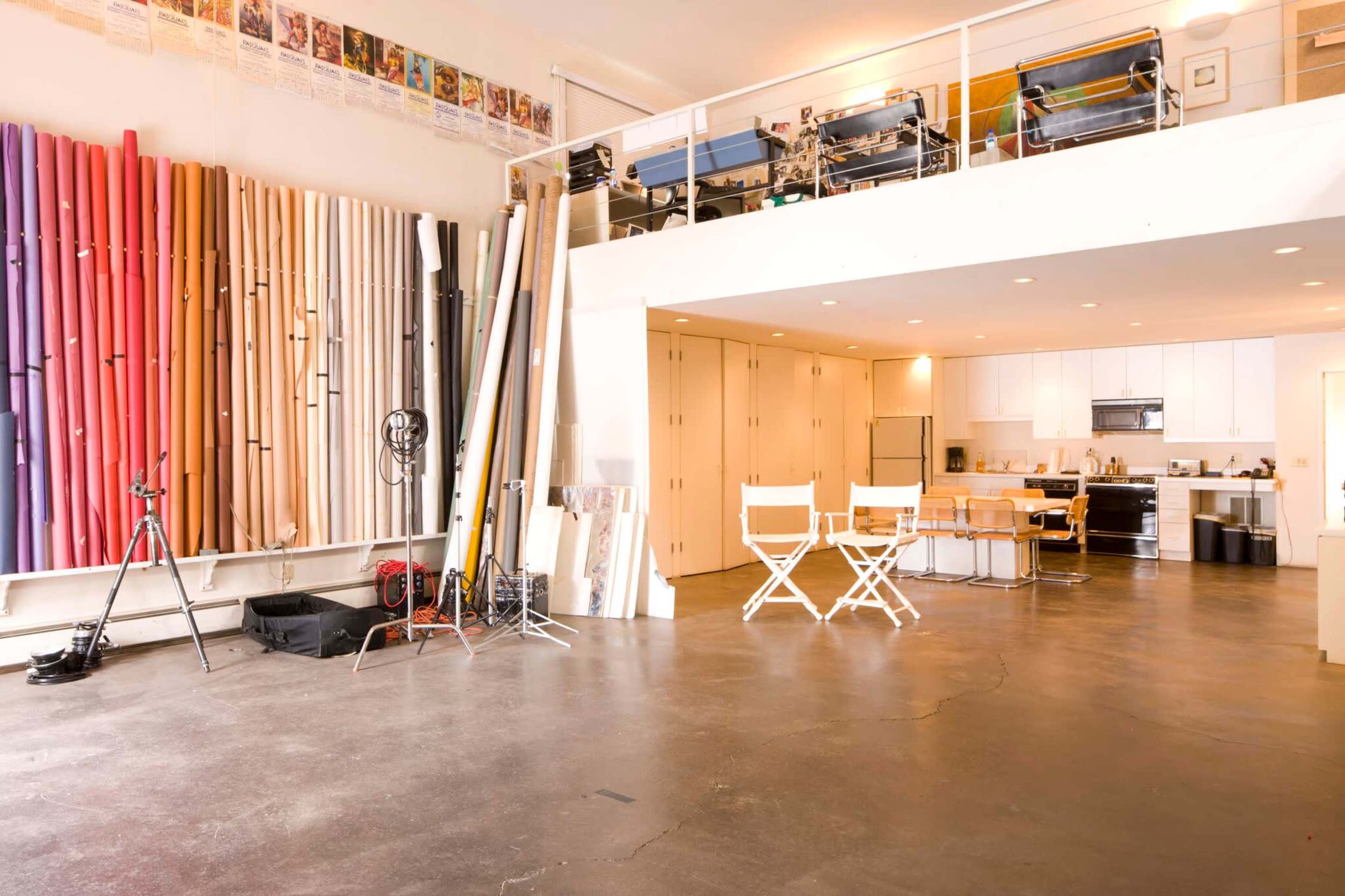 A spacious studio with a variety of colored backdrops against one wall and a kitchen area along with a dining table and chairs in the center.