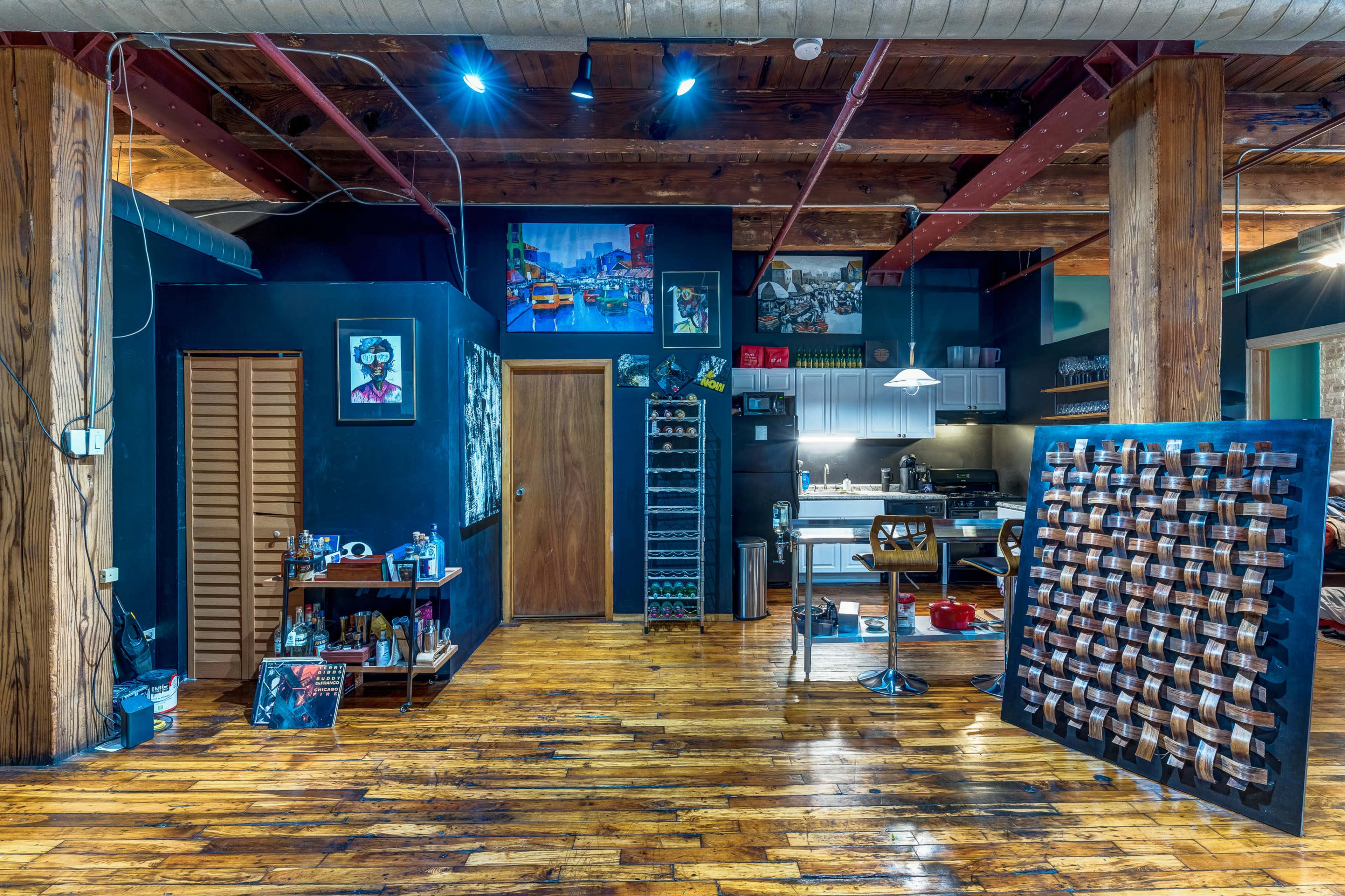 A modern loft with wooden floors, exposed beams, and a kitchen visible in the background, adorned with various artworks and decor.