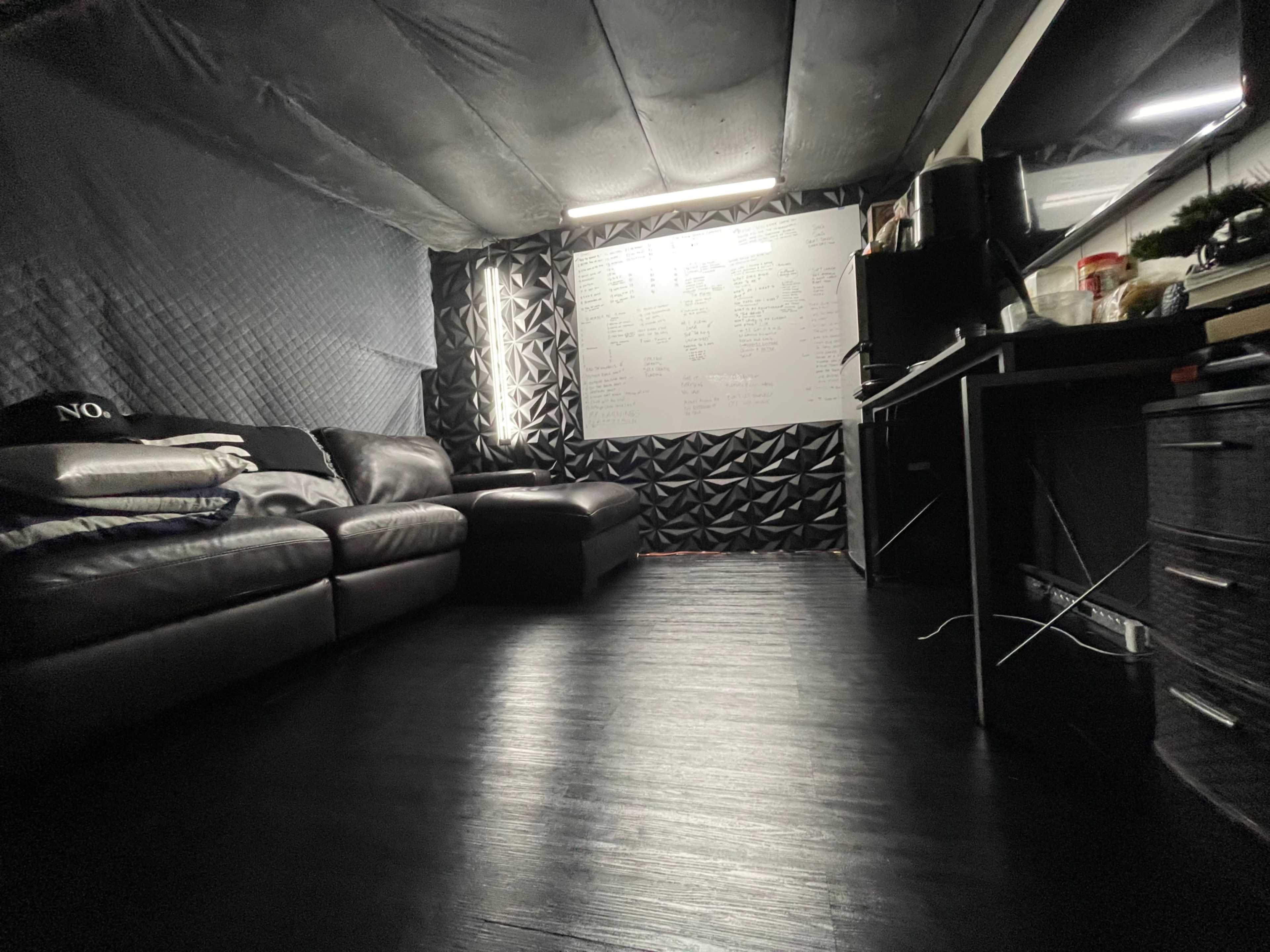 The image shows a room with dark walls, a leather couch, an ottoman, and a whiteboard filled with writing.
